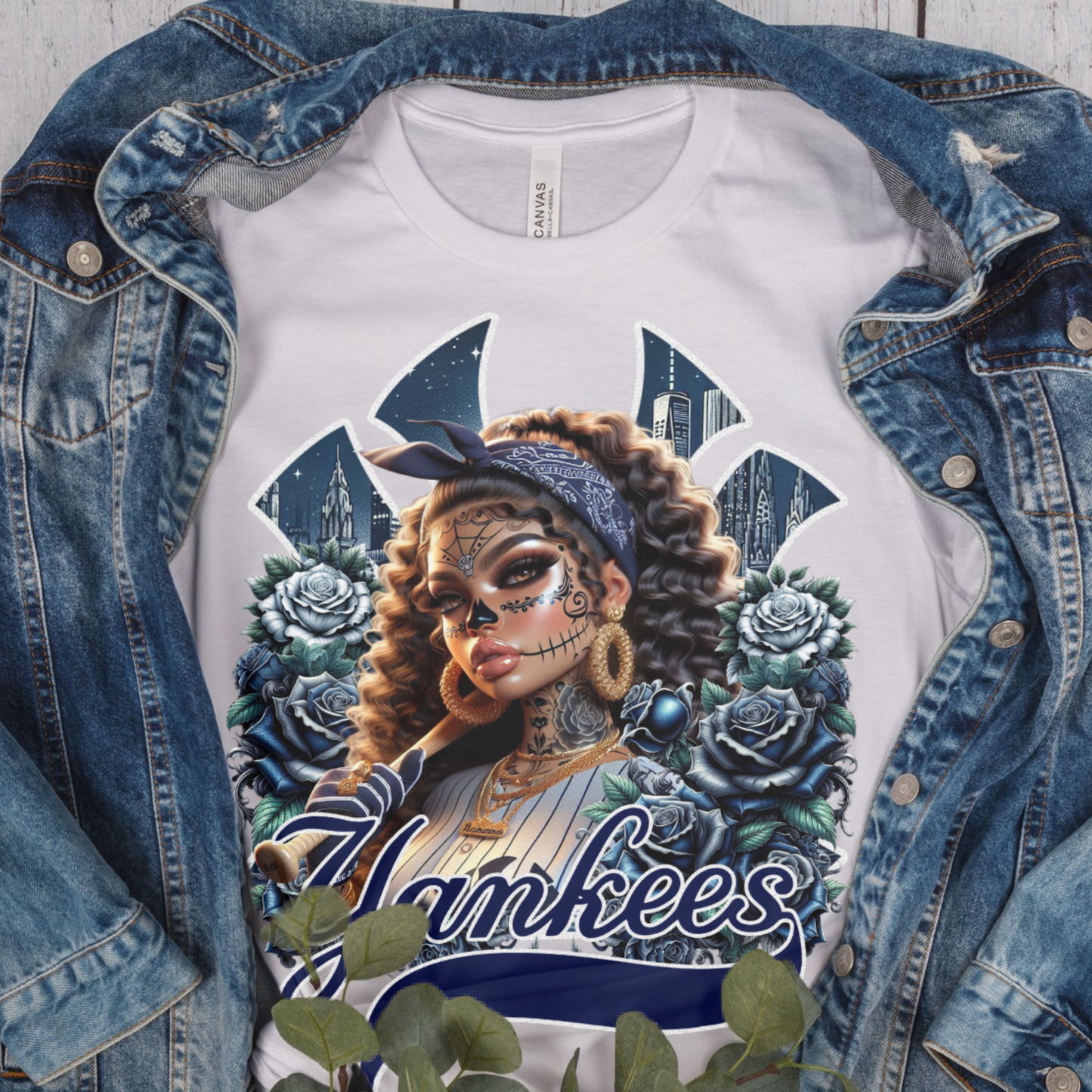 White t-shirt with dia de los muertos 'Yankees' design featuring a woman with tattoos and flowers, displayed with a denim jacket.