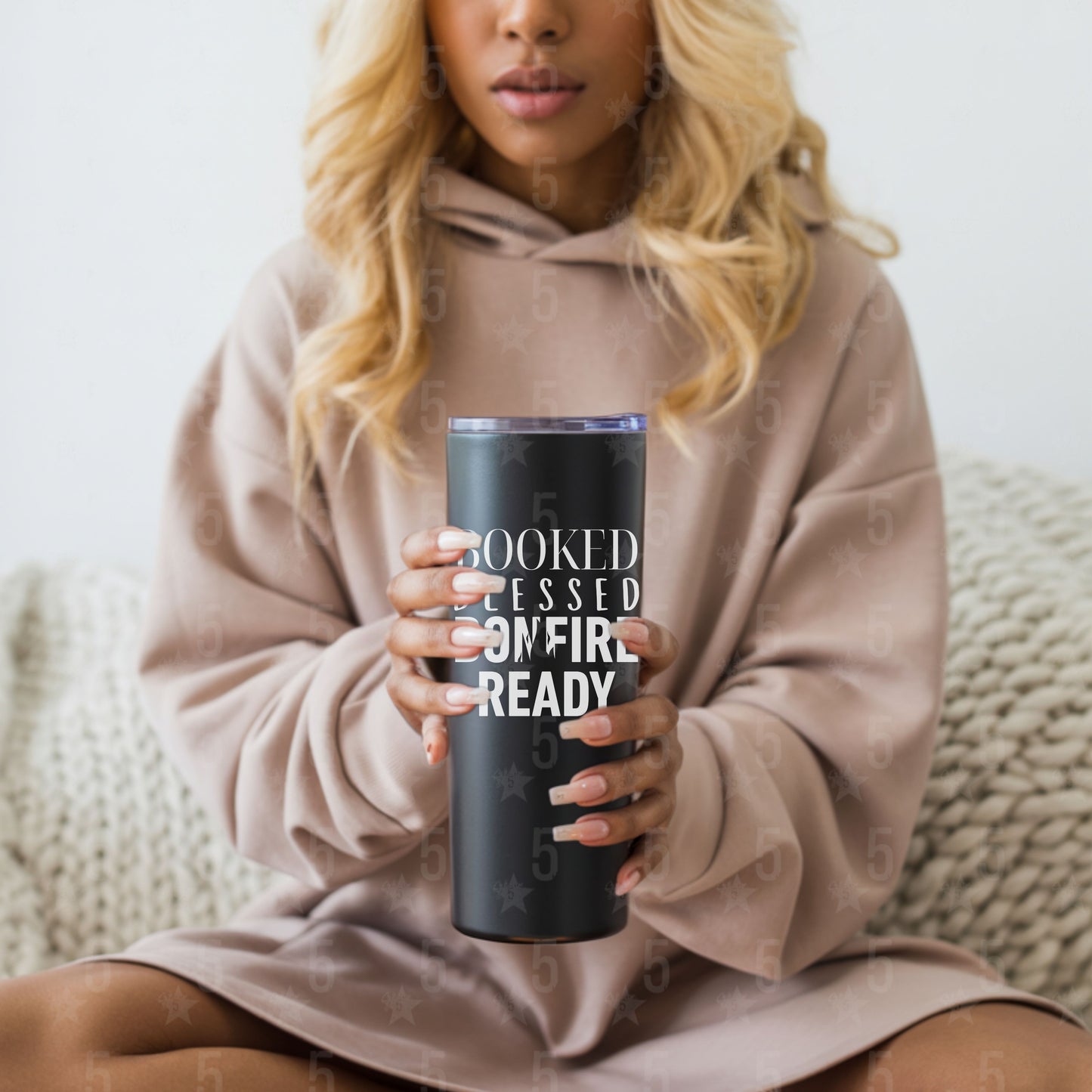 Person holding a tumbler with text design, sitting on a couch.