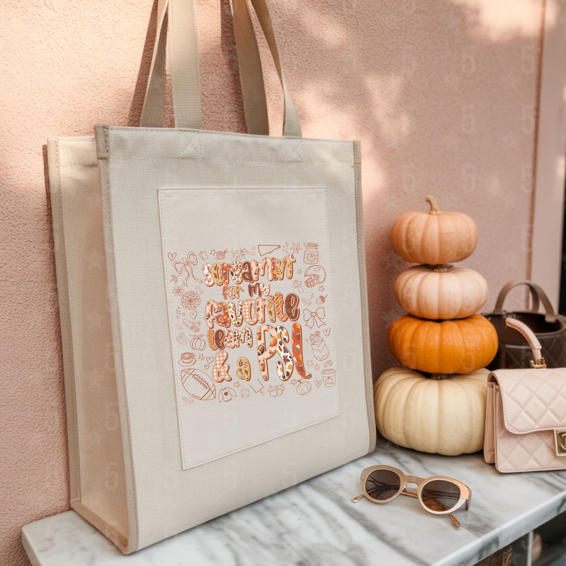 Beige tote bag with decorative text, sunglasses, and pumpkins on a marble surface.