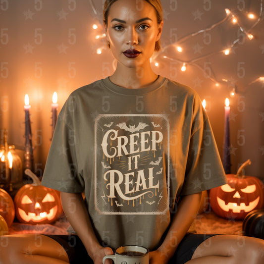 Woman wearing a 'Creep It Real' t-shirt in a Halloween-themed setting with pumpkins and string lights.