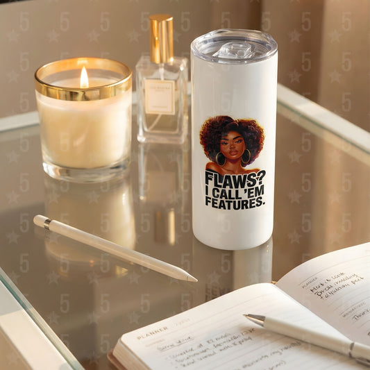 Tumbler with a motivational quote on a reflective surface with a candle and pen.