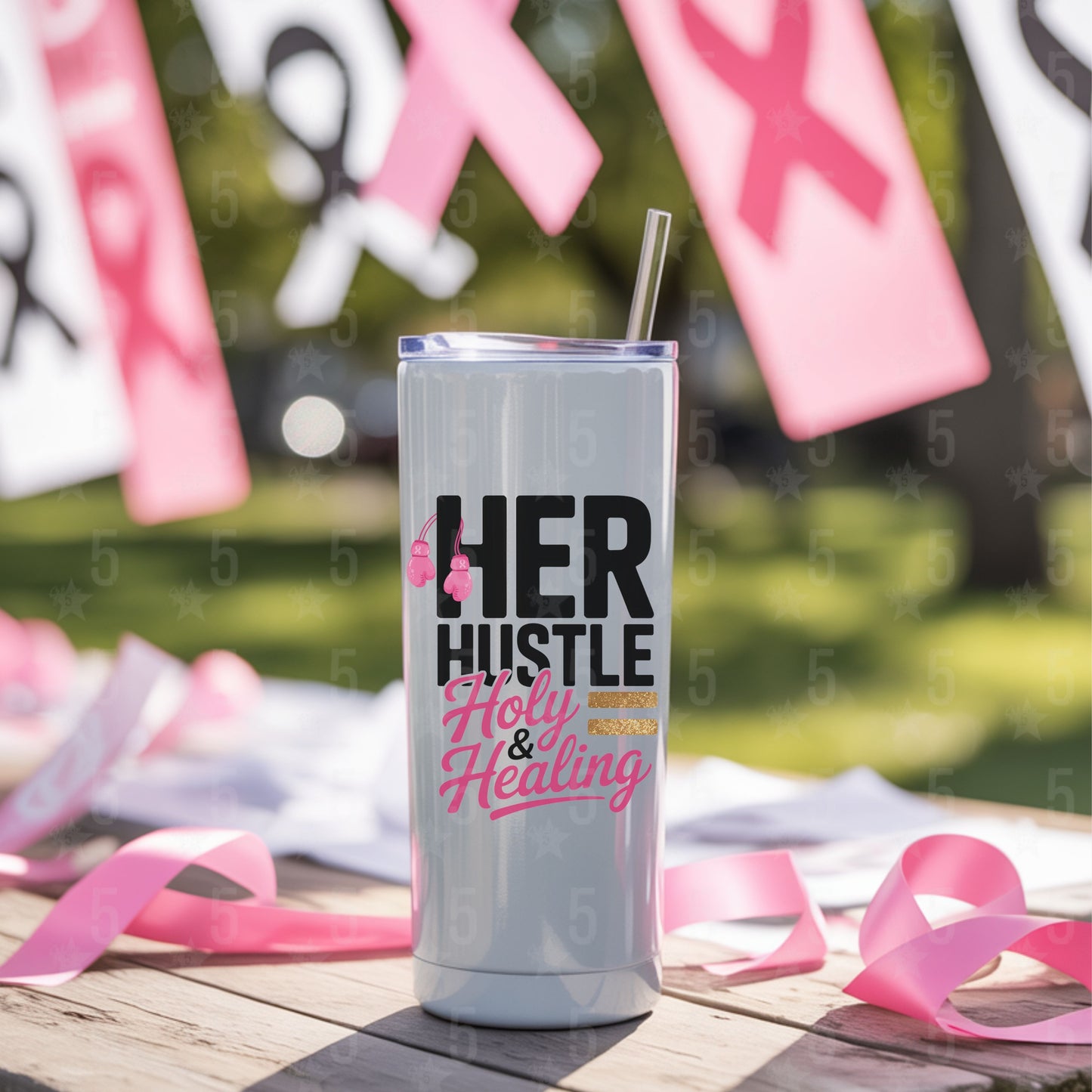Tumbler with 'HER HUSTLE Holy & Healing' text surrounded by pink ribbons on a blurred outdoor background