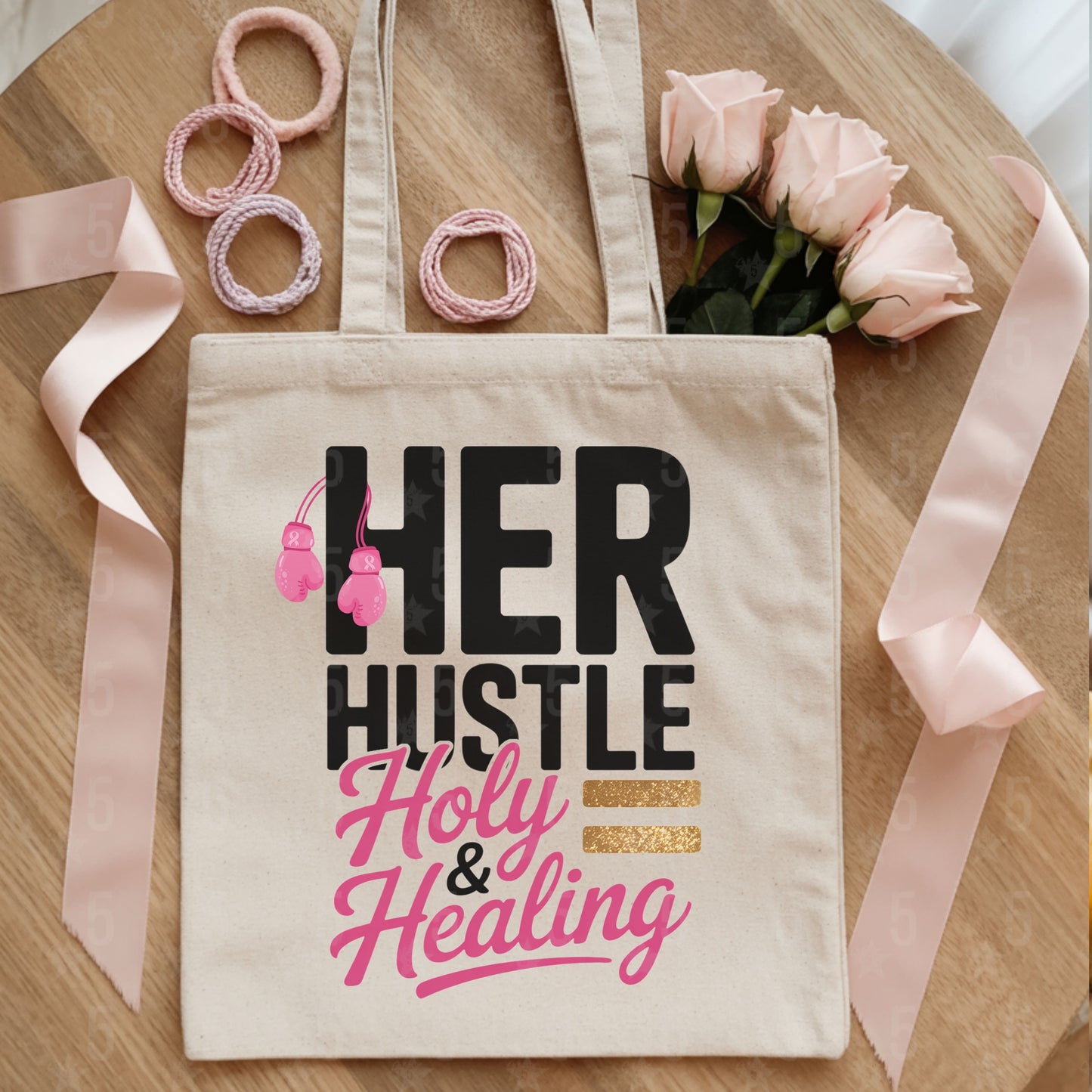 Tote bag with 'HER HUSTLE Holy & Healing' text on a wooden surface with ribbons and flowers.