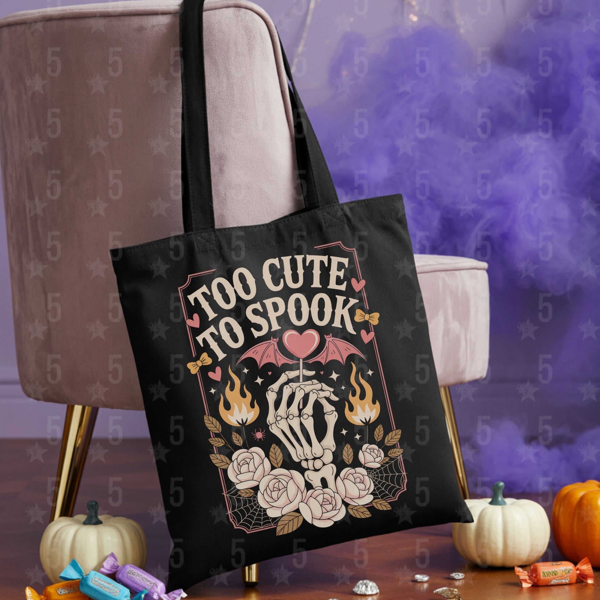 Black tote bag with skeleton design and 'Too Cute To Spook' text on a decorative background with pumpkins and candy.