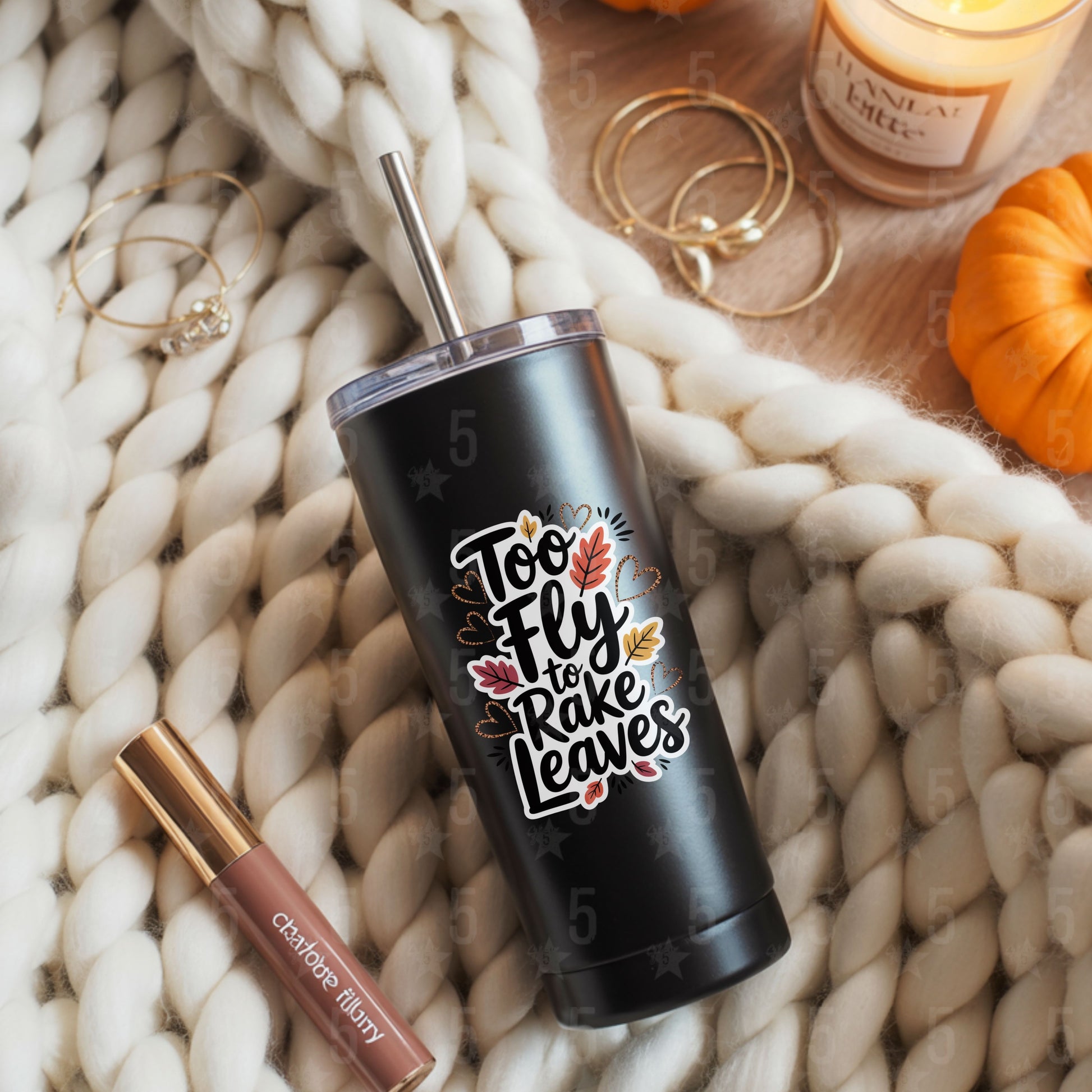 Black tumbler with 'Too Fly to Rake Leaves' design on a textured surface with lip gloss and earrings.