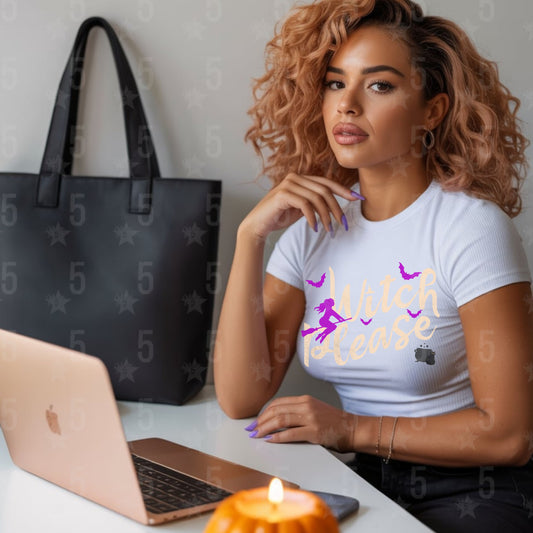 Woman sitting at a desk with a laptop, wearing a white t-shirt with text, next to a black handbag and lit candle.
