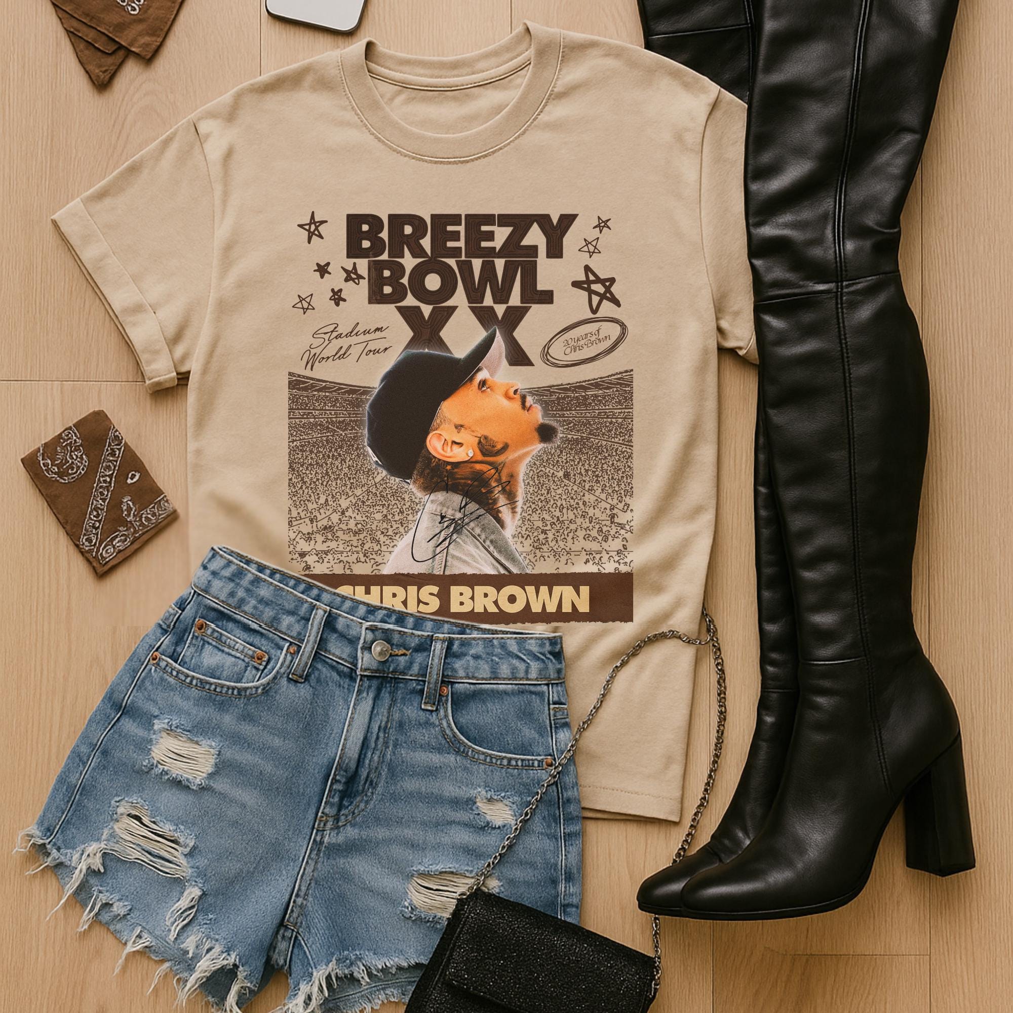 Beige t-shirt with with Breezy Bowl graphic, denim shorts, black boots, and wallet on a wooden surface