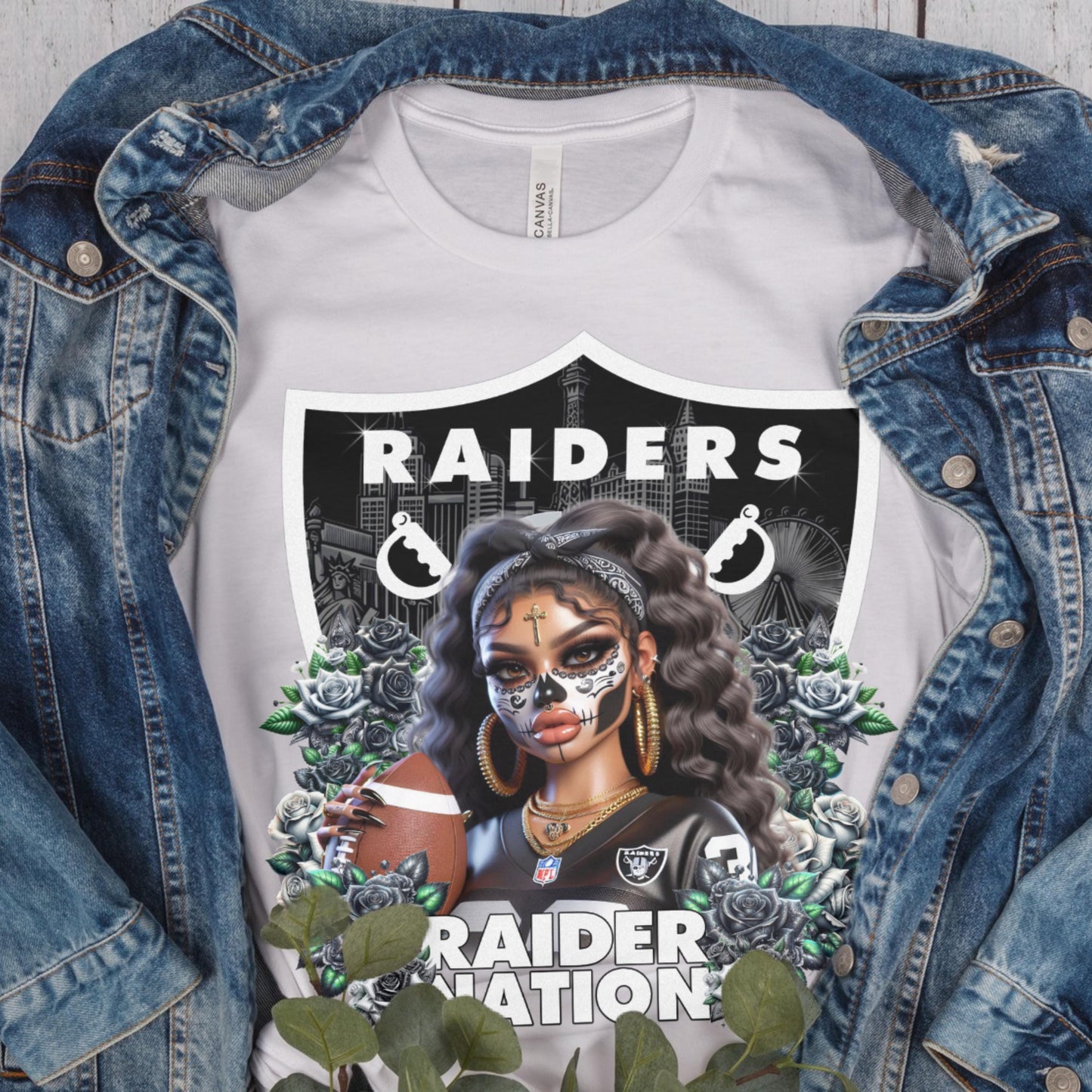White t-shirt with a dia de los muertos Raiders design, displayed inside a denim jacket.