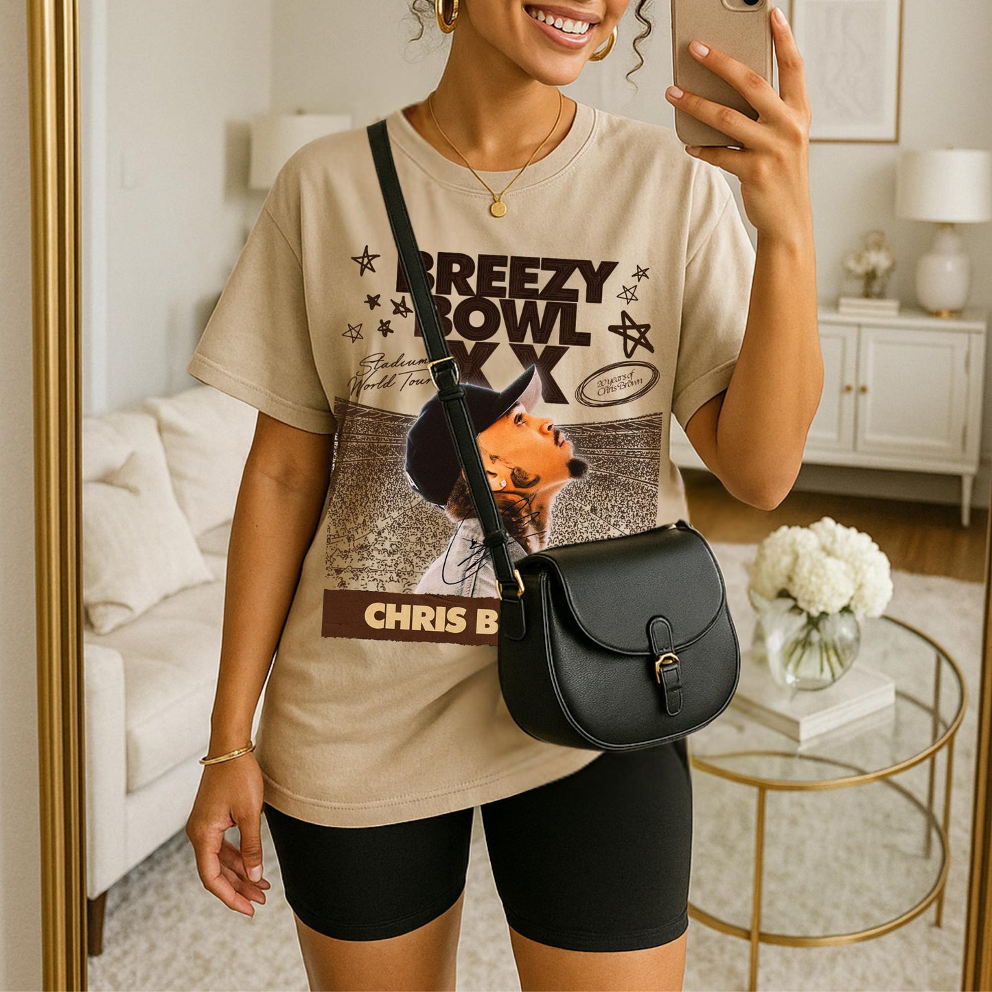 Person wearing a graphic t-shirt with with Breezy Bowl graphic, holding a phone, standing in a room.