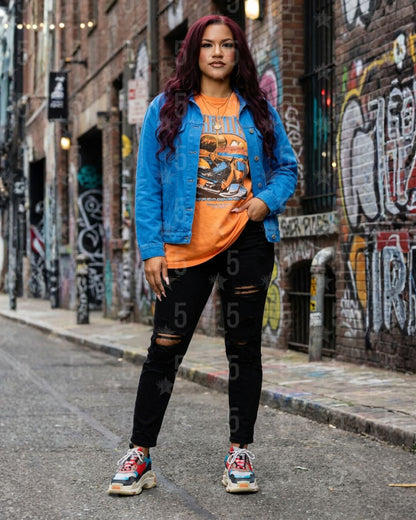 Person wearing a blue jacket, orange shirt, and black pants standing in an urban alley with graffiti.