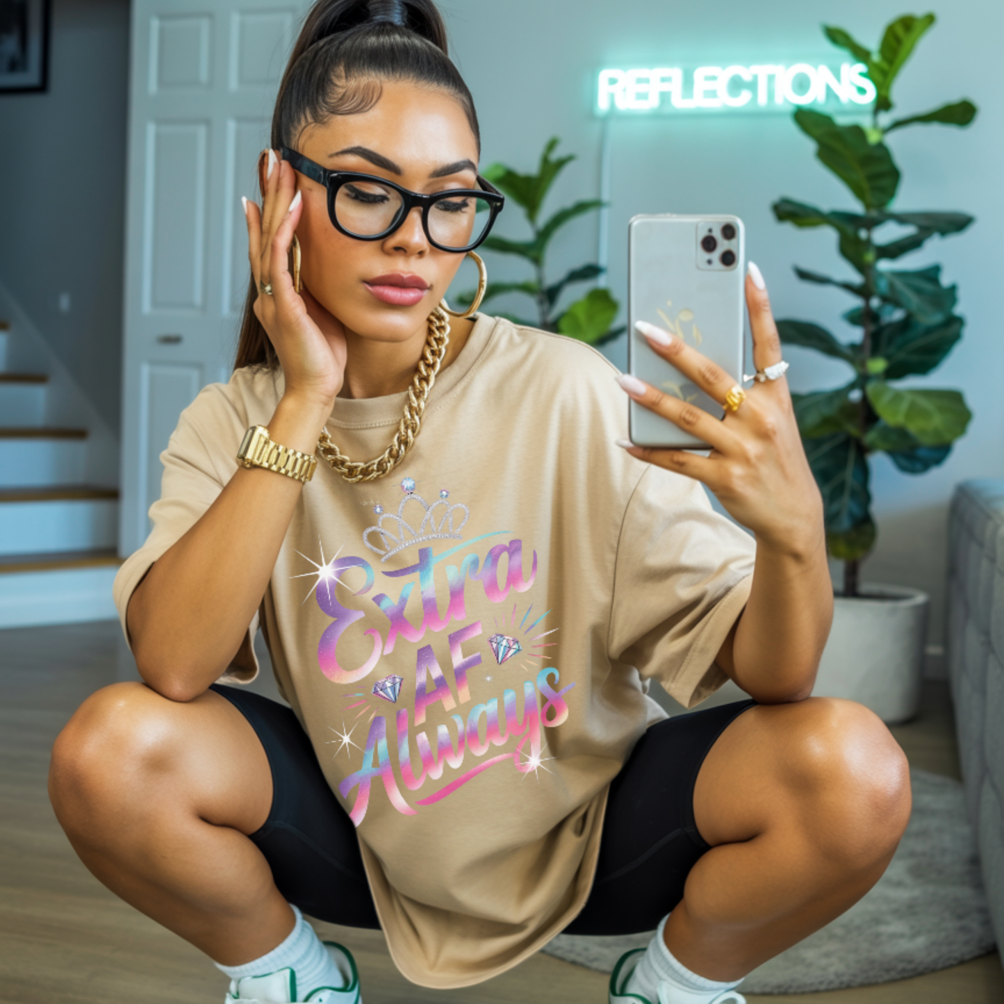Woman taking a mirror selfie wearing a beige oversized shirt with colorful text, sitting on the floor.