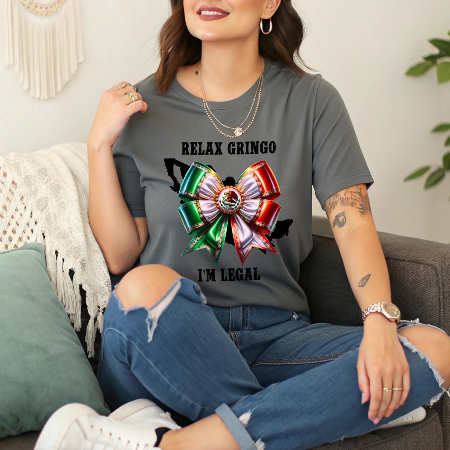 Person wearing a gray t-shirt with a Mexican bow and Relax Gringo I'm Legal text, sitting on a couch.