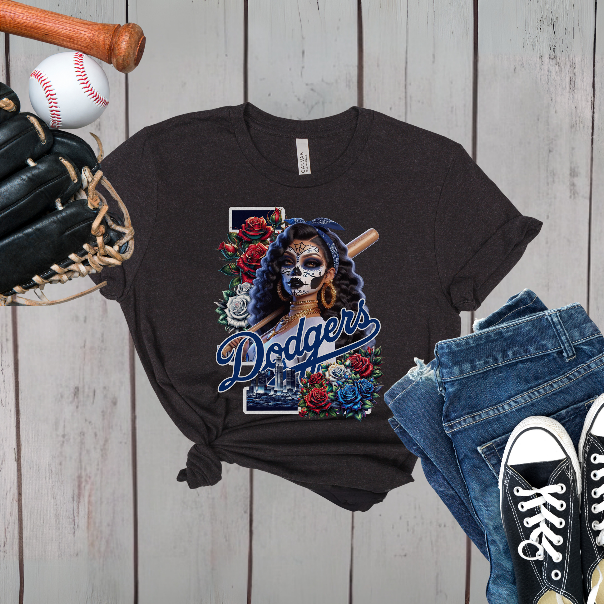 Black t-shirt with 'Dodgers'  dia de los muertos design, baseball glove, baseball, jeans, and sneakers on a wooden background