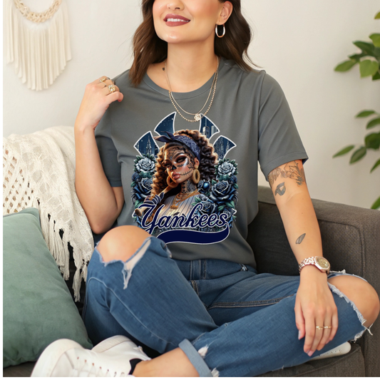 Woman wearing a t-shirt with a dia de los muertos 'Yankees' design and floral design, sitting on a couch.