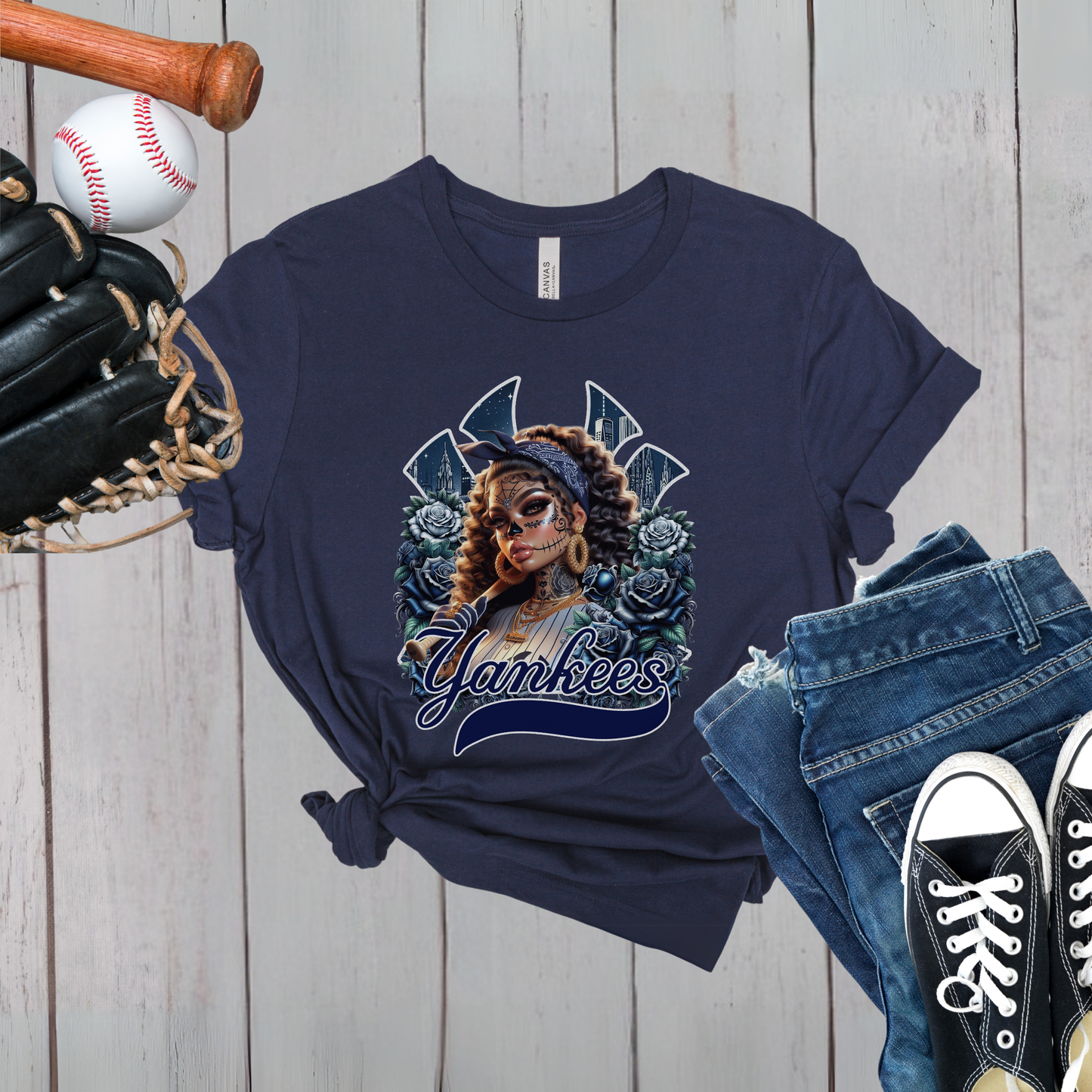 Navy blue t-shirt with dia de los muertos 'Yankees' design, baseball, bat, glove, and jeans on a wooden surface