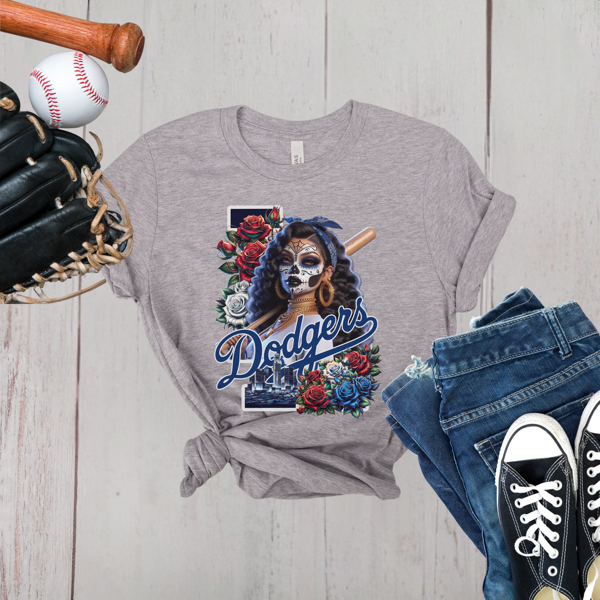 Gray t-shirt with Dodgers dia de los muertos design, surrounded by baseball equipment on a wooden surface.