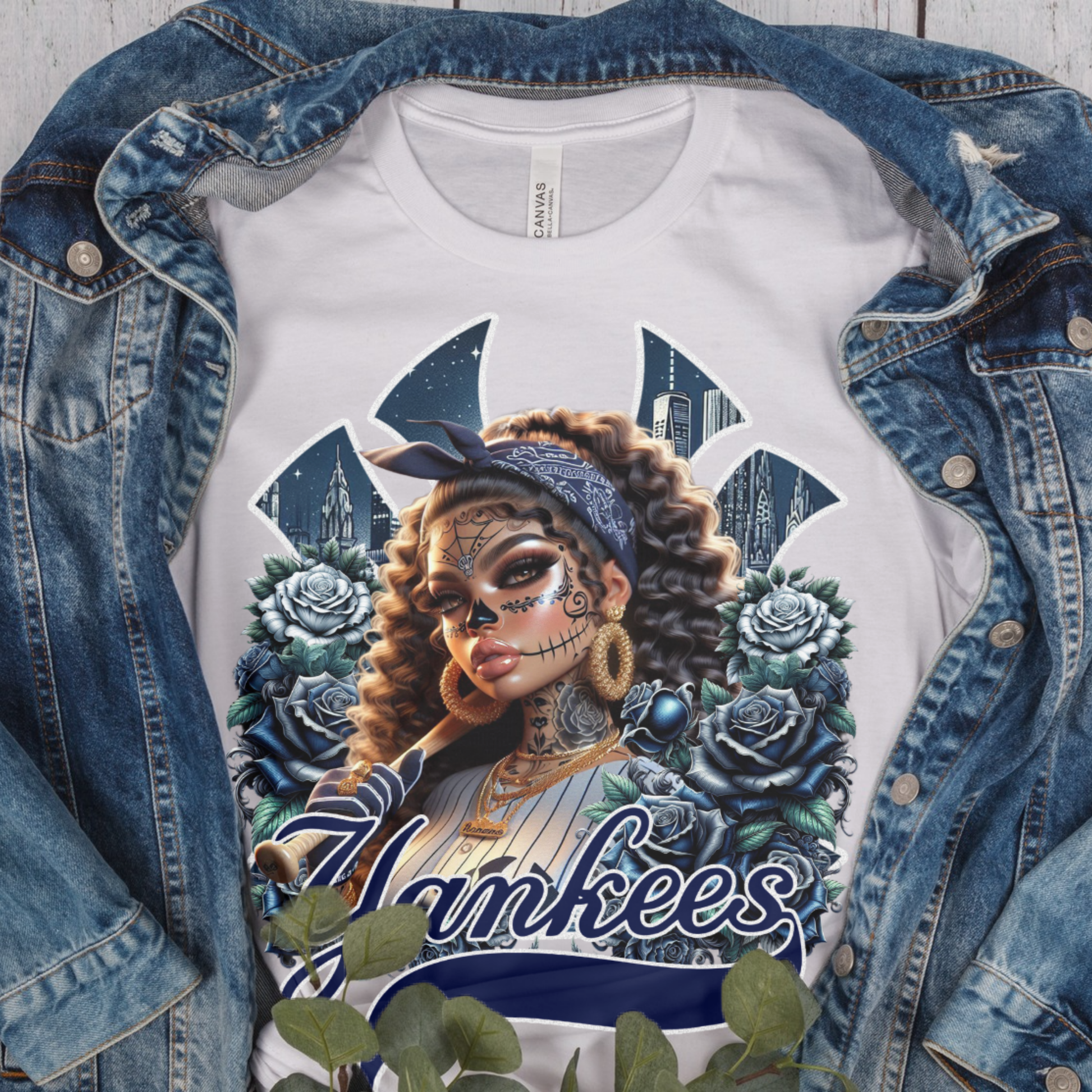 White t-shirt with dia de los muertos 'Yankees' design featuring a woman with tattoos and flowers, displayed with a denim jacket.