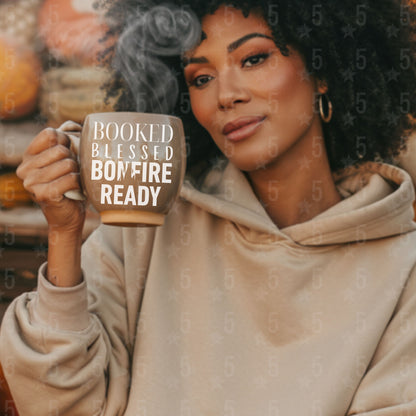 Woman holding a mug with 'Booked Blessed Bonfire Ready' text, surrounded by autumn decorations.