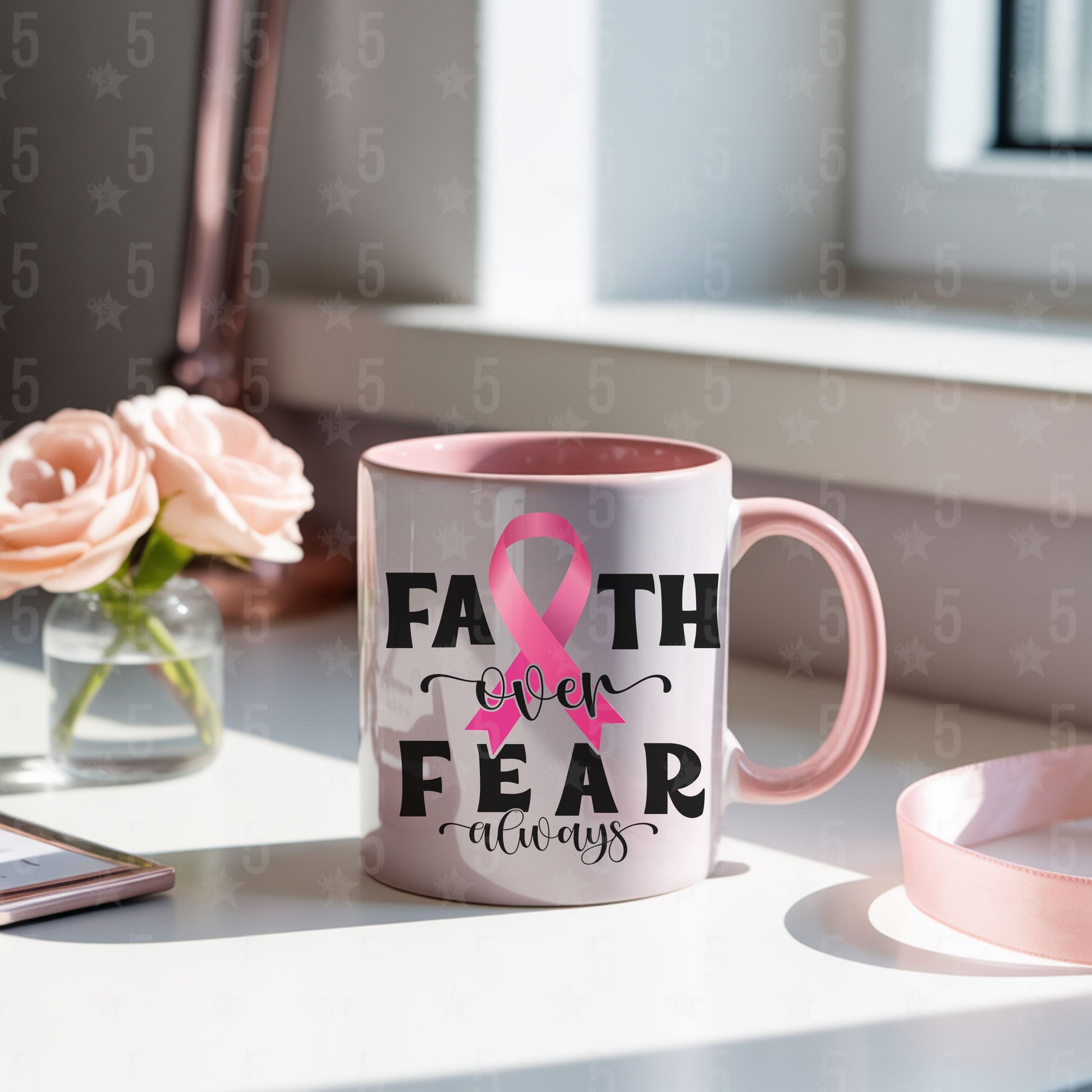 Mug with pink ribbon and 'Faith over Fear always' text on a desk with flowers and a phone.