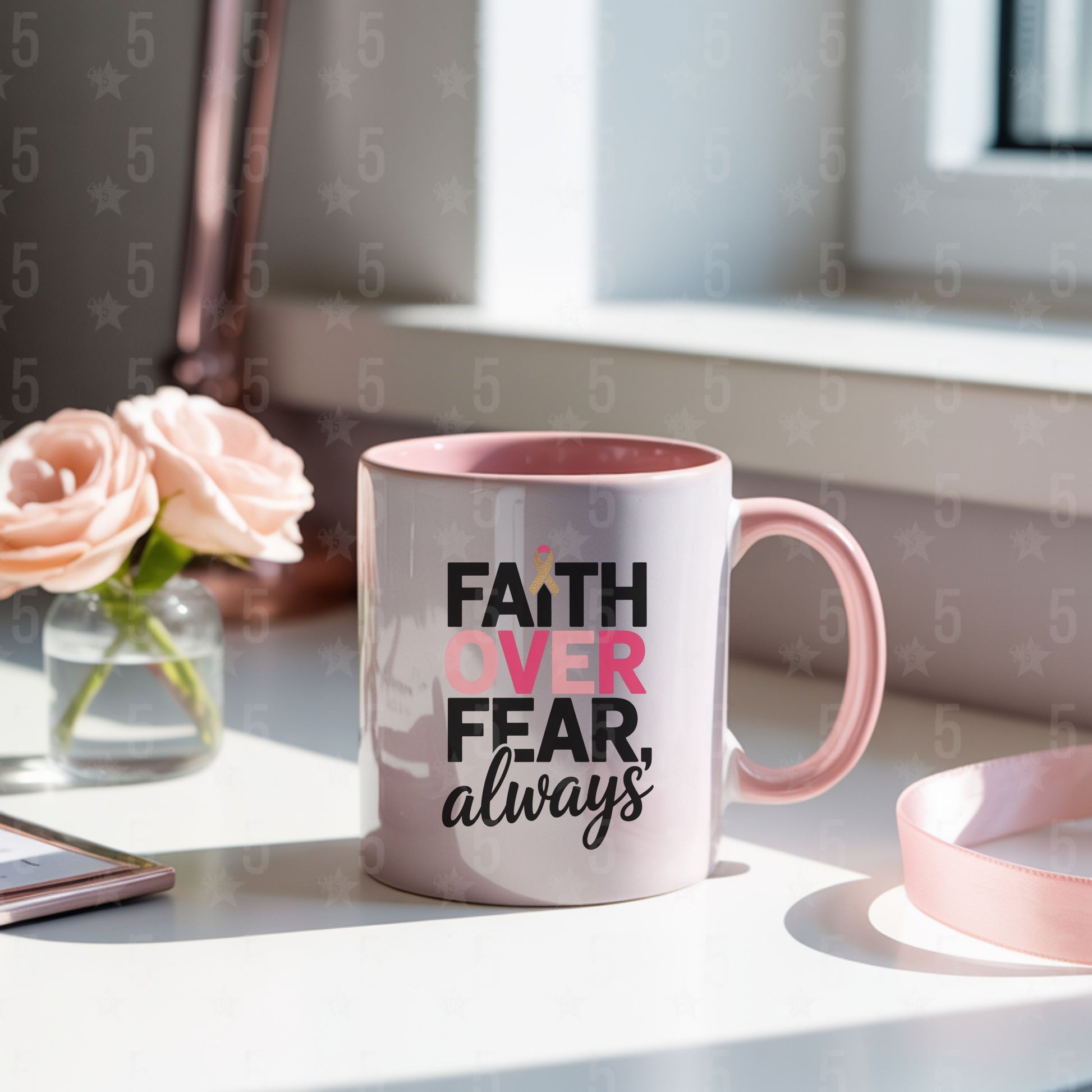 Pink mug with 'Faith Over Fear, always' text on a desk with flowers and a phone.