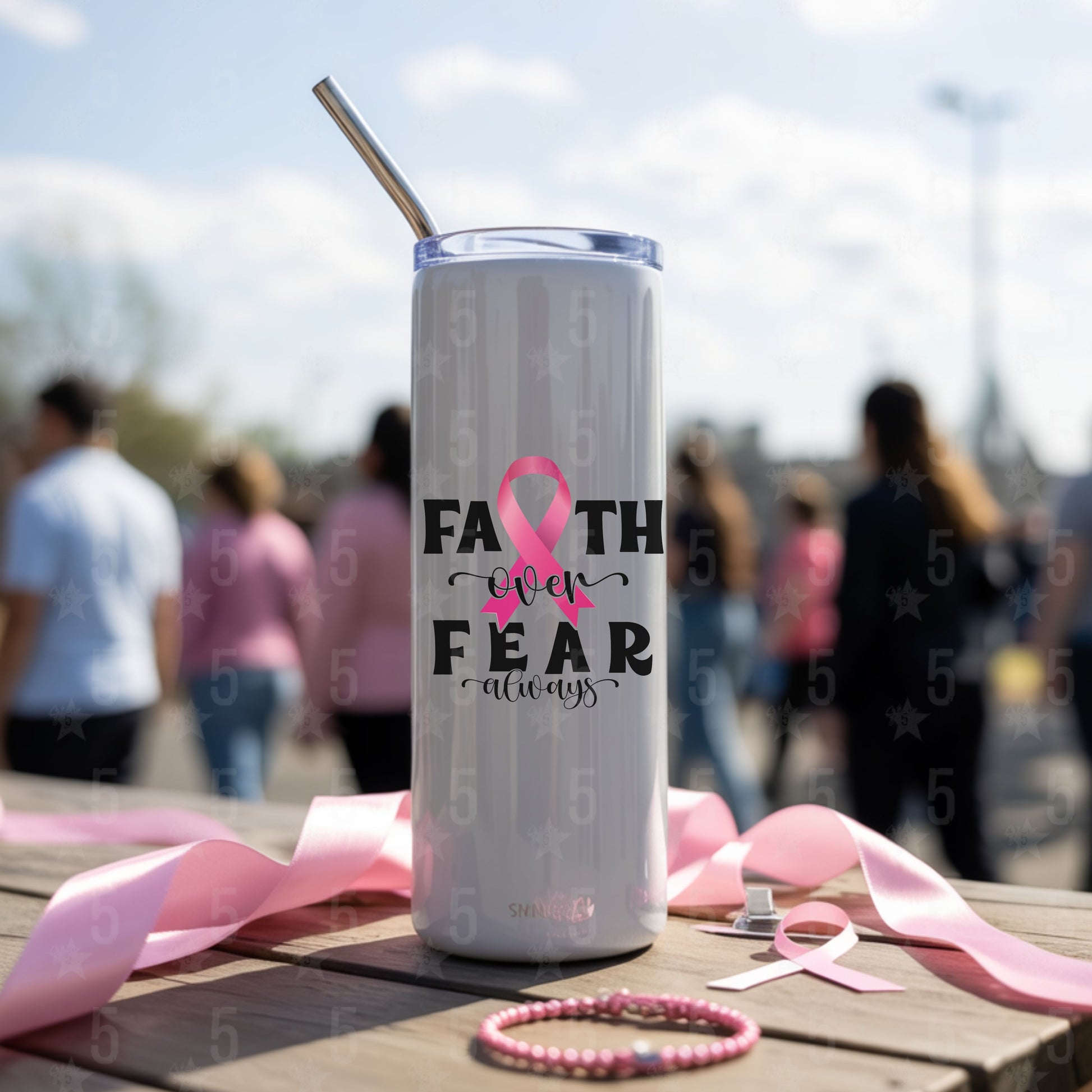 Tumbler with pink ribbon and 'Faith over Fear' text on a table with blurred people in the background