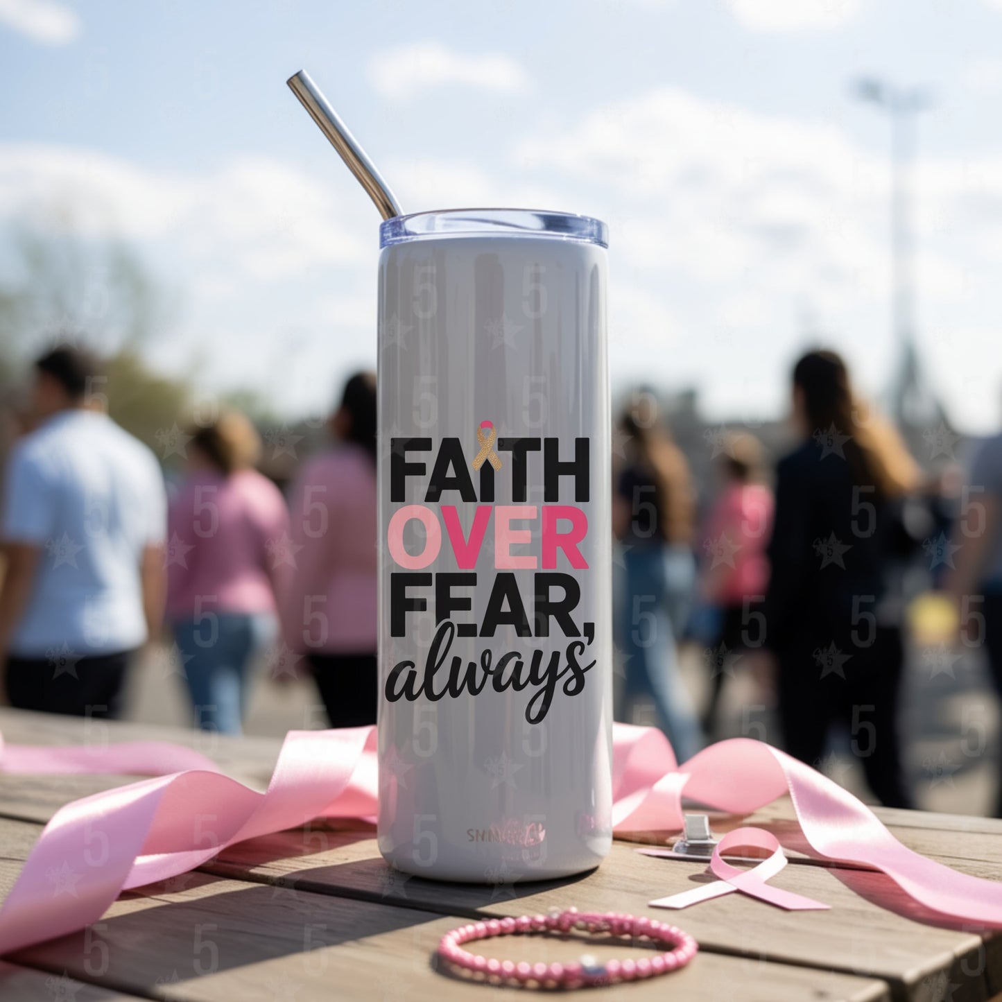 Tumbler with 'Faith Over Fear, always' text on a wooden table with pink ribbons and a blurred outdoor background.