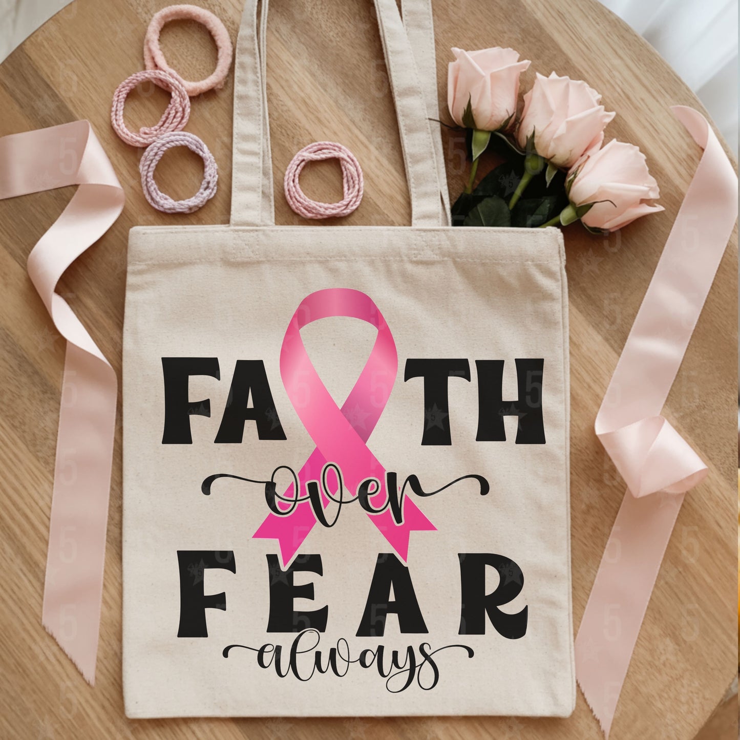 Tote bag with pink ribbon and text on a wooden surface with ribbons and flowers.