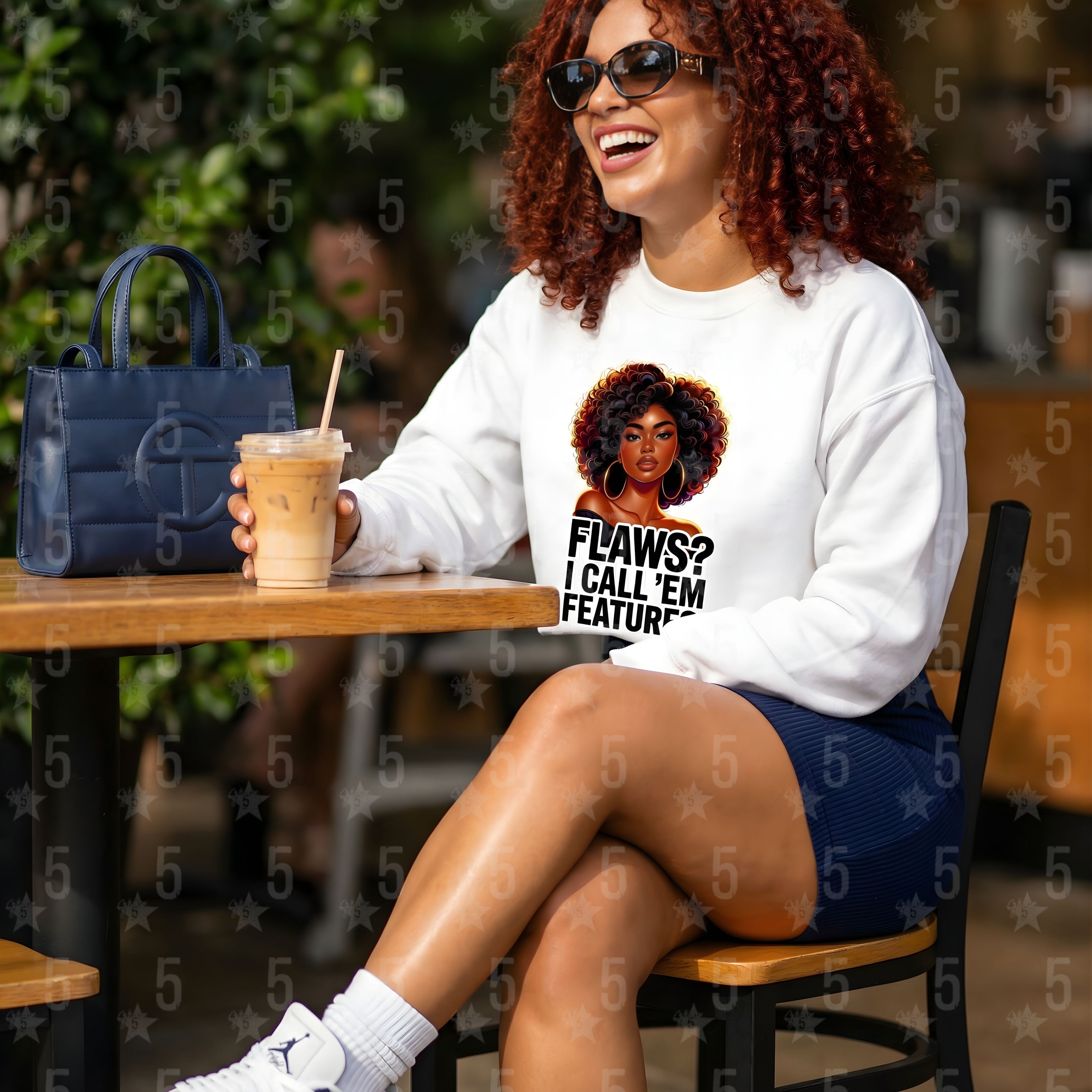 Woman sitting at a table outdoors, wearing a white sweatshirt with a graphic design.