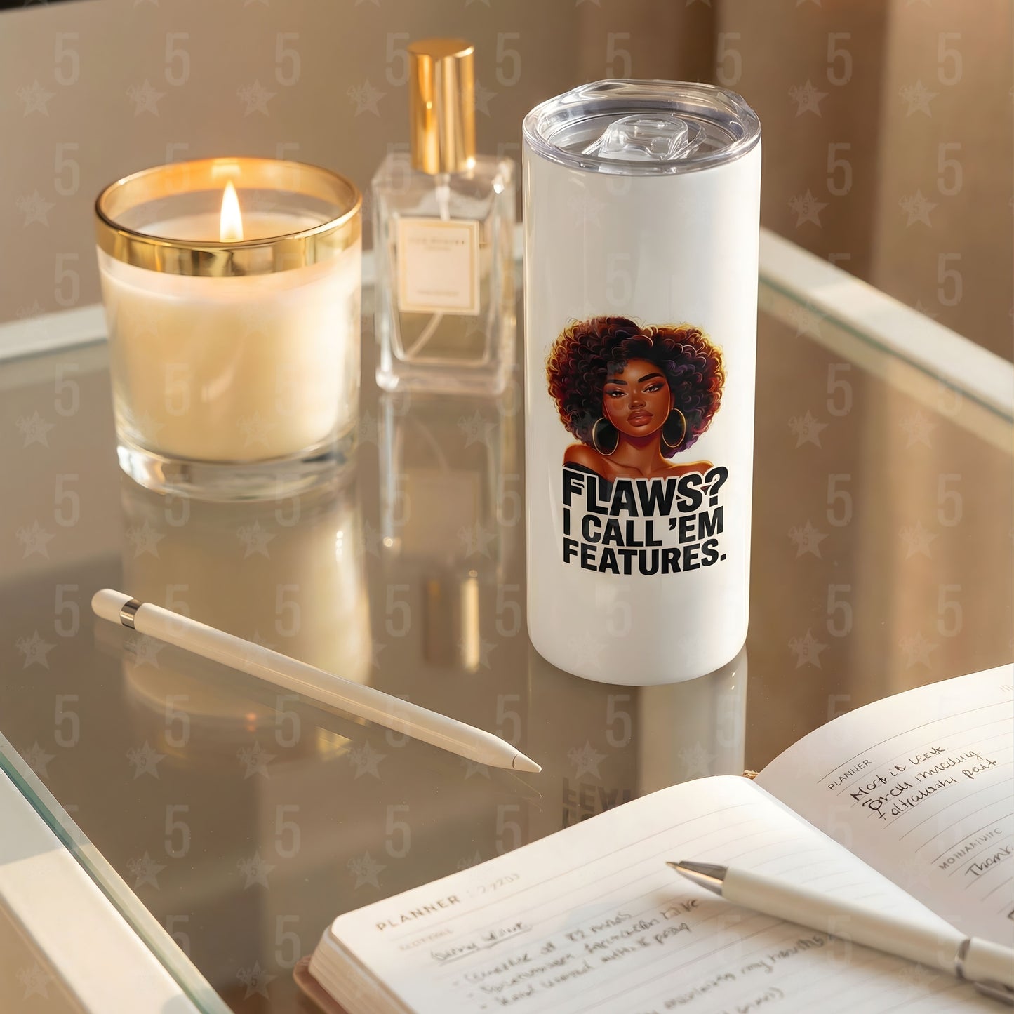 Tumbler with a motivational quote on a reflective surface with a candle and pen.