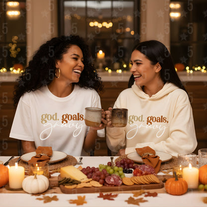 Two women sitting at a festive table with 'god, goals, glory' shirts, surrounded by pumpkins and candles.