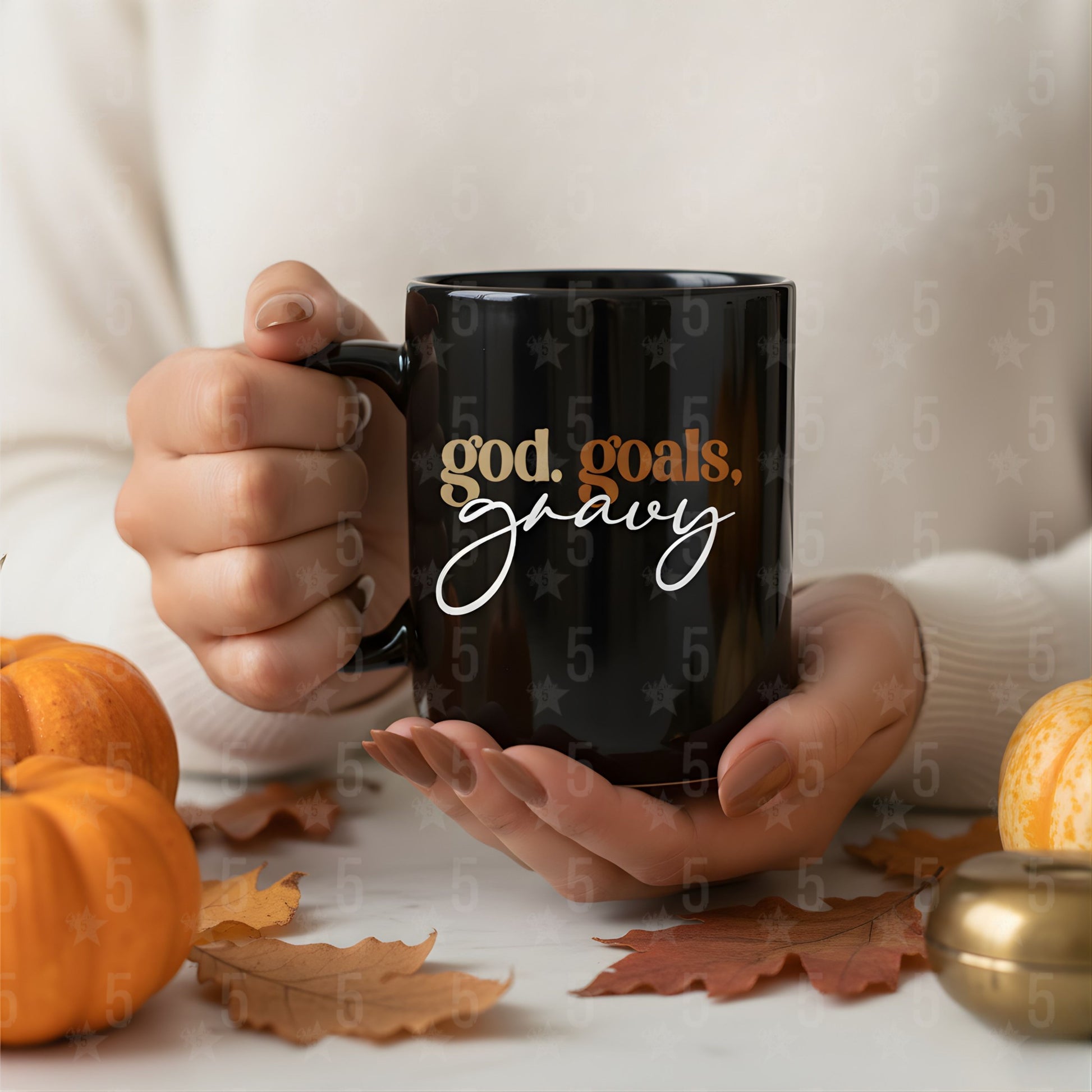 Person holding a black mug with 'god. goals. gravy' text, surrounded by pumpkins and leaves.