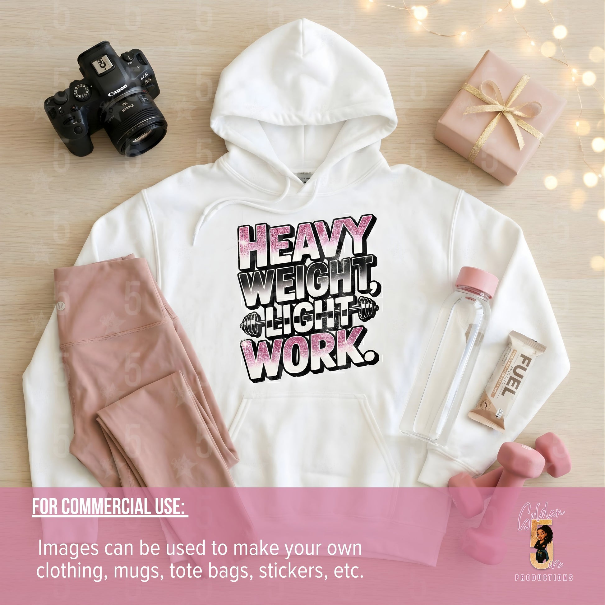 White hoodie with 'Heavy Weight Light Work' text, camera, gift box, and water bottle on a wooden surface.