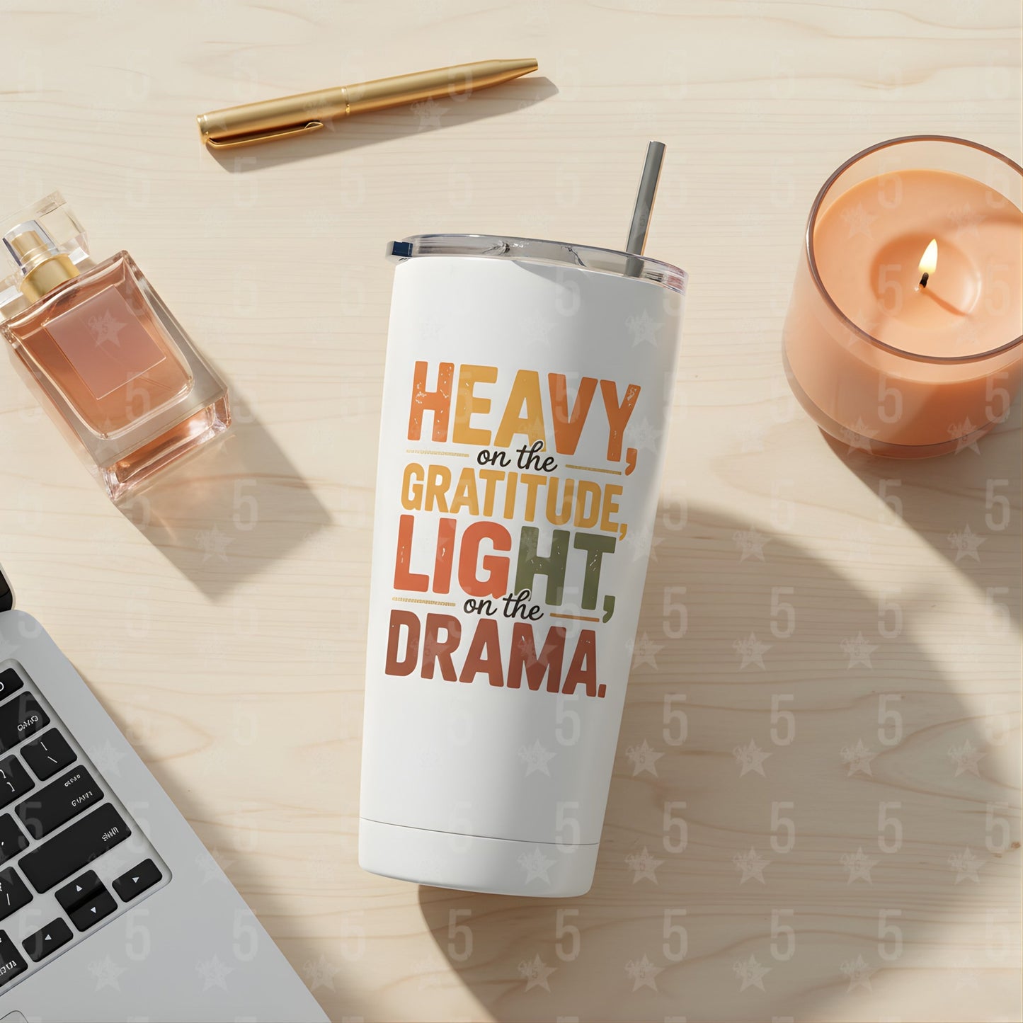 Tumbler with motivational quote on a desk with laptop, candle, and perfume bottle.