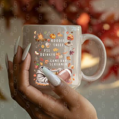 Mug with autumn-themed text and graphics held by a hand with painted nails.