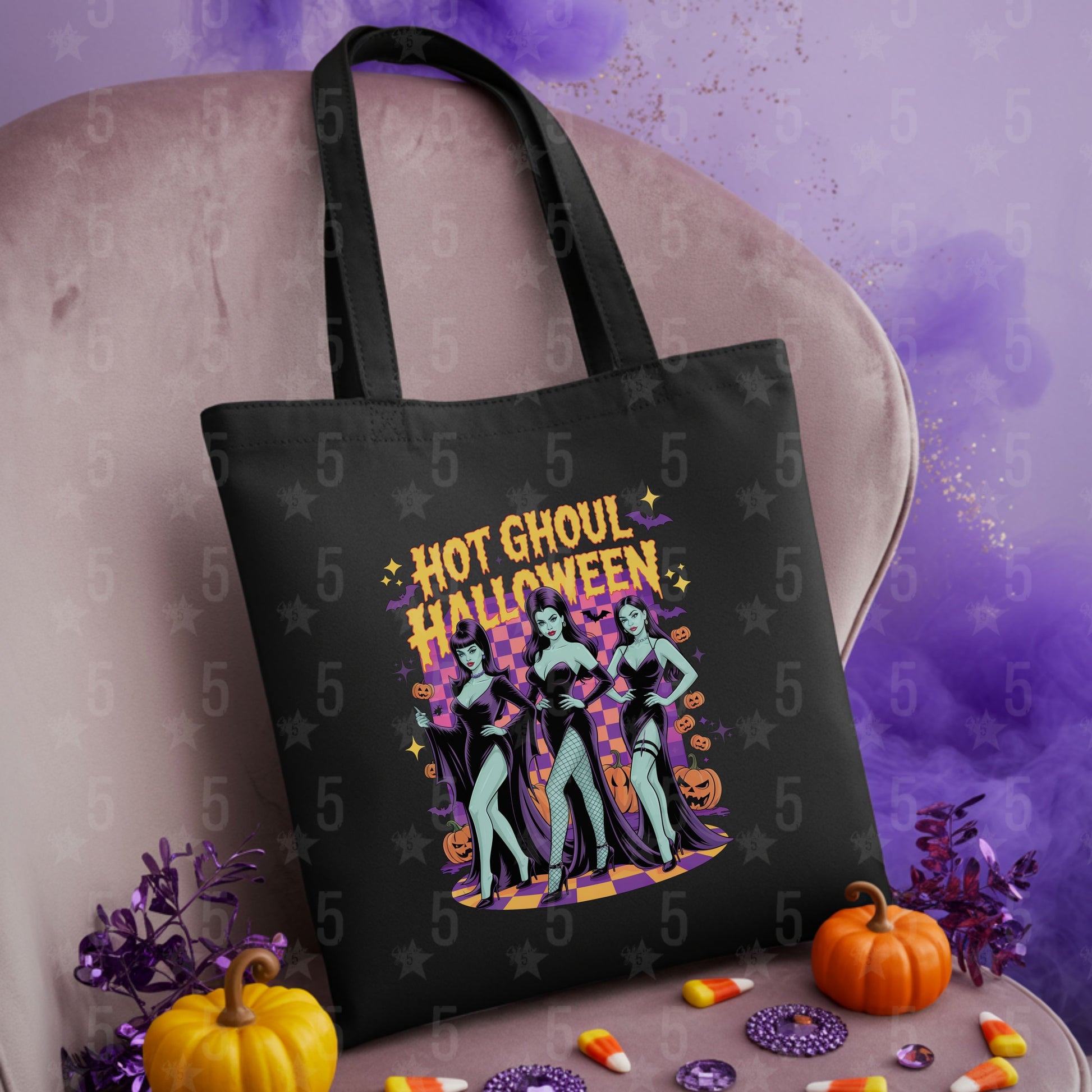 Black tote bag with Halloween design featuring two women and text, placed on a textured surface with pumpkins and candy.