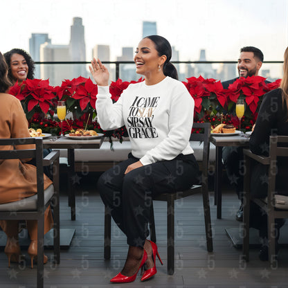 Woman in a white sweatshirt with text sitting at a table with red poinsettias and city skyline in the background.