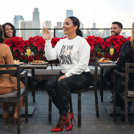 Woman in a white sweatshirt with text sitting at a table with red poinsettias and city skyline in the background.