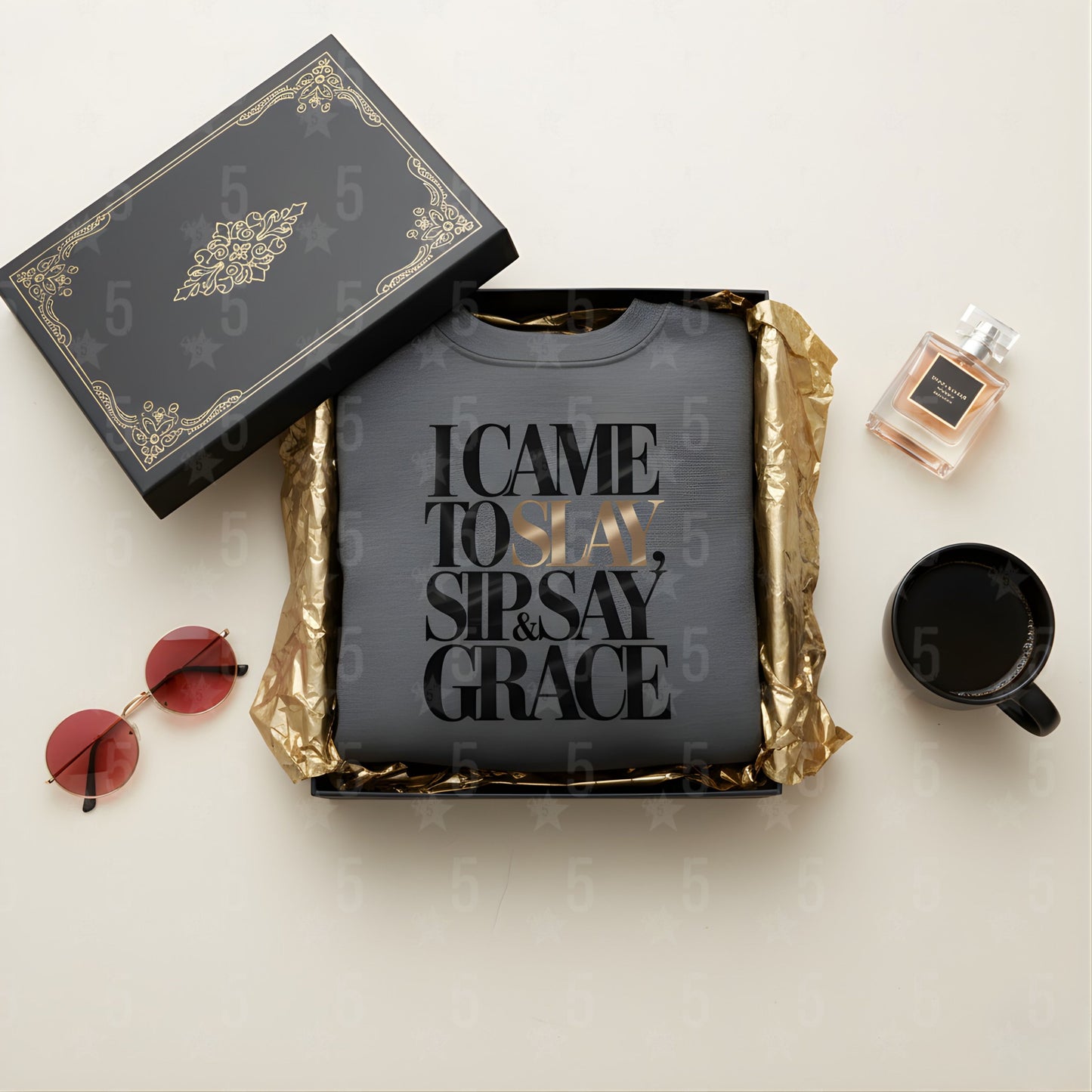 Black t-shirt with text, sunglasses, mug, and perfume bottle on a light surface