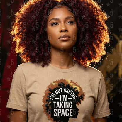 Woman wearing a beige t-shirt with a graphic and text, standing against a dark background.