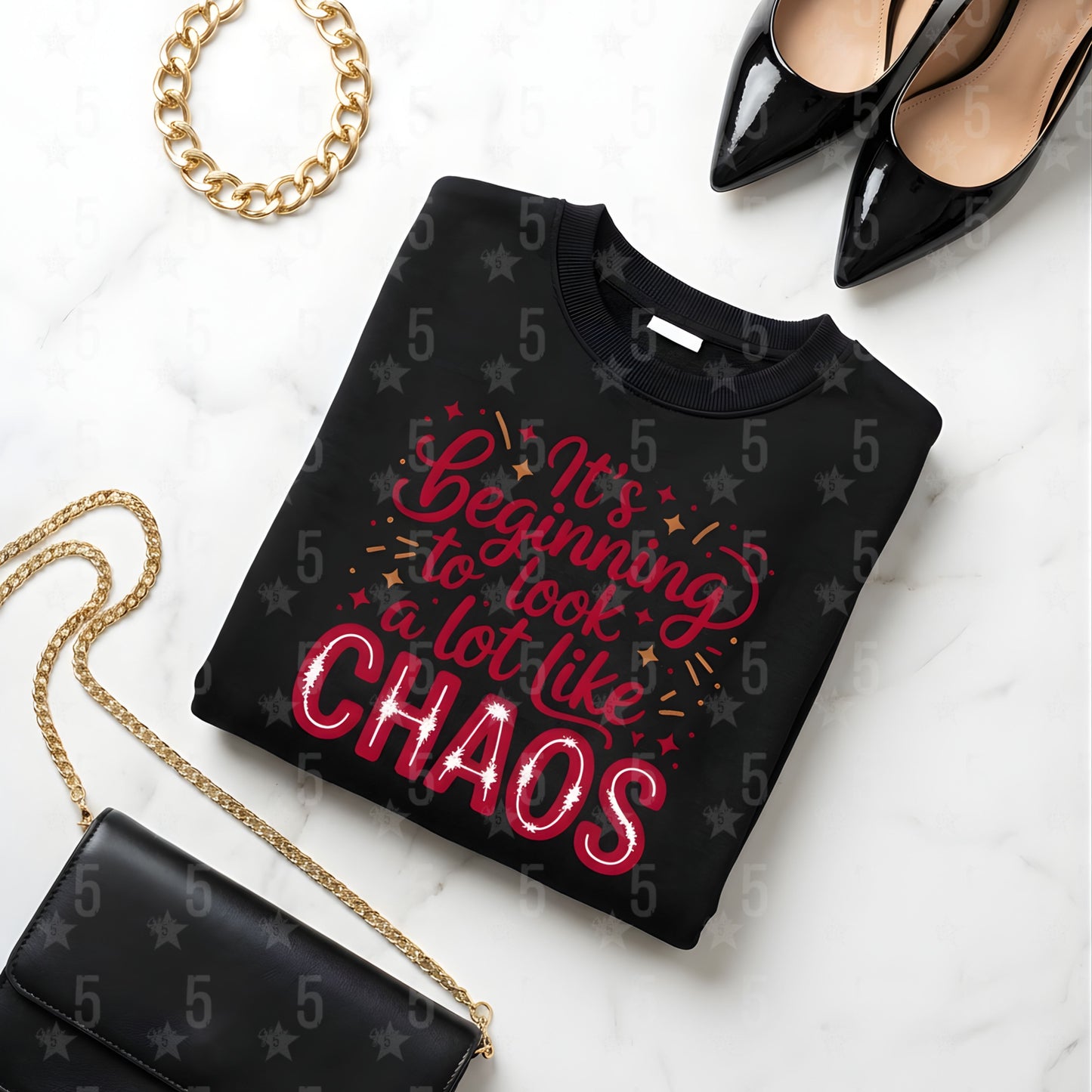 Black sweatshirt with red text 'It's Beginning to look a lot like CHAOS', black high heels, gold chain, and black handbag on a white marble surface.