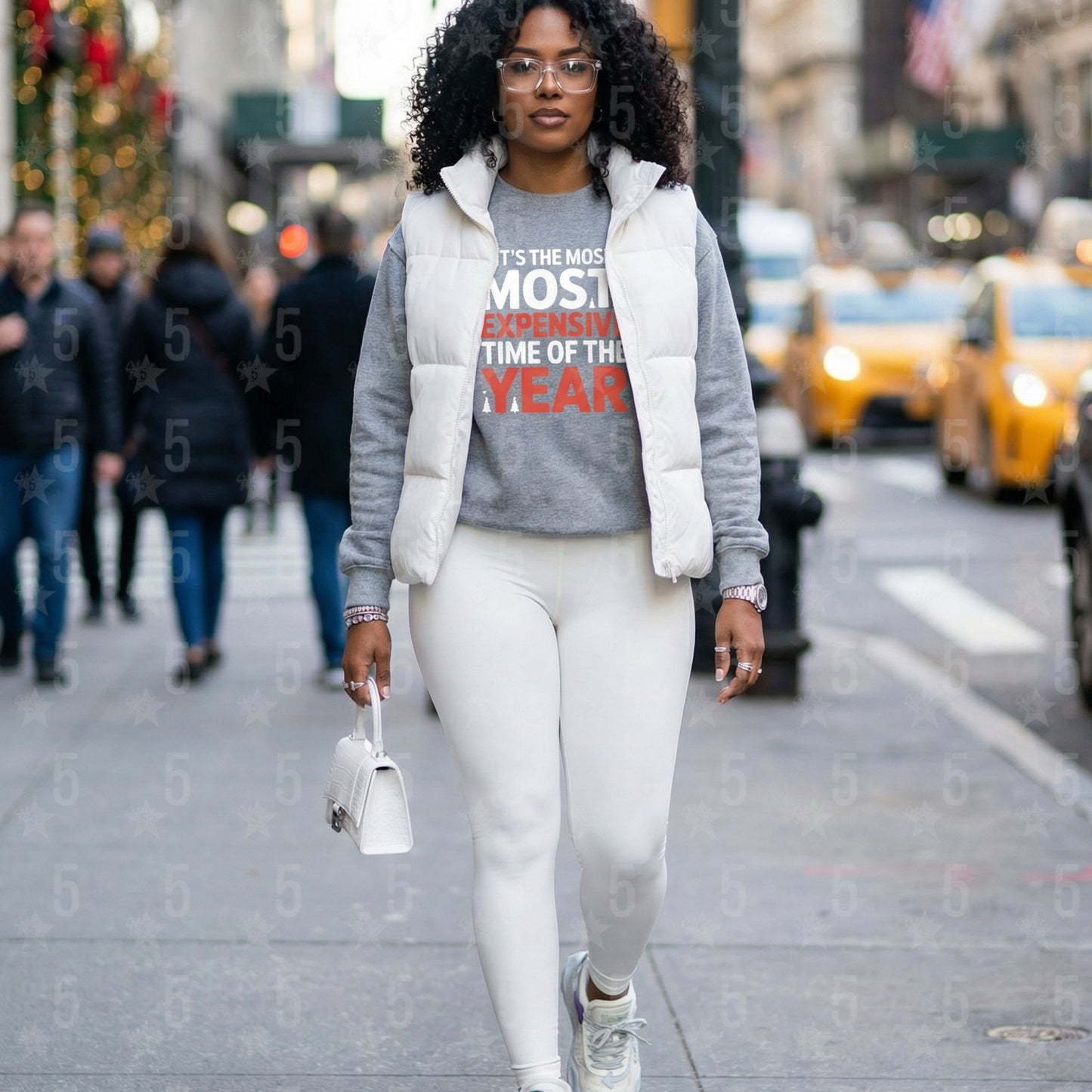 Woman walking on a city street wearing a gray sweatshirt with text and a white puffer vest.