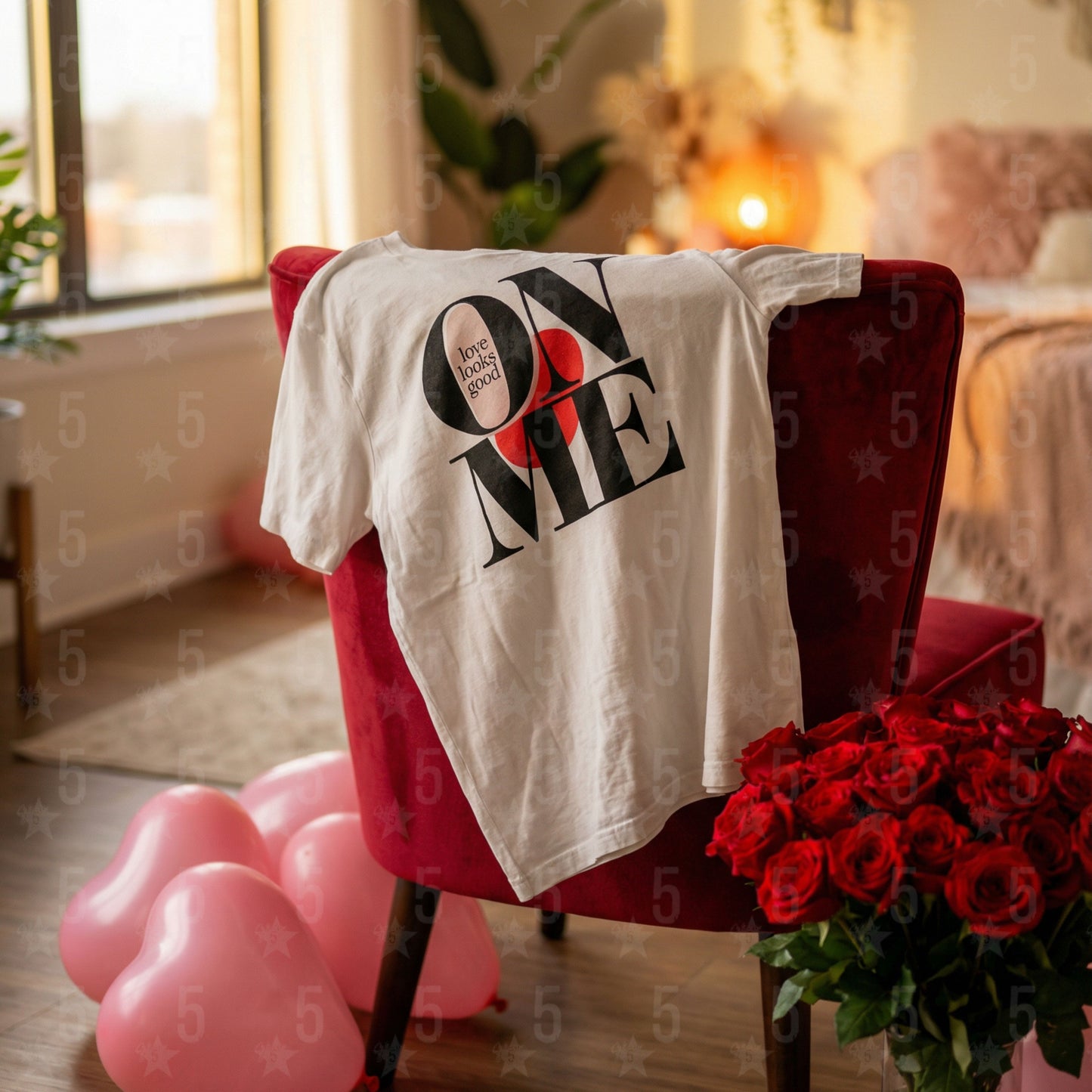 White t-shirt with 'ON ME' text on a red chair with balloons and flowers in a room.