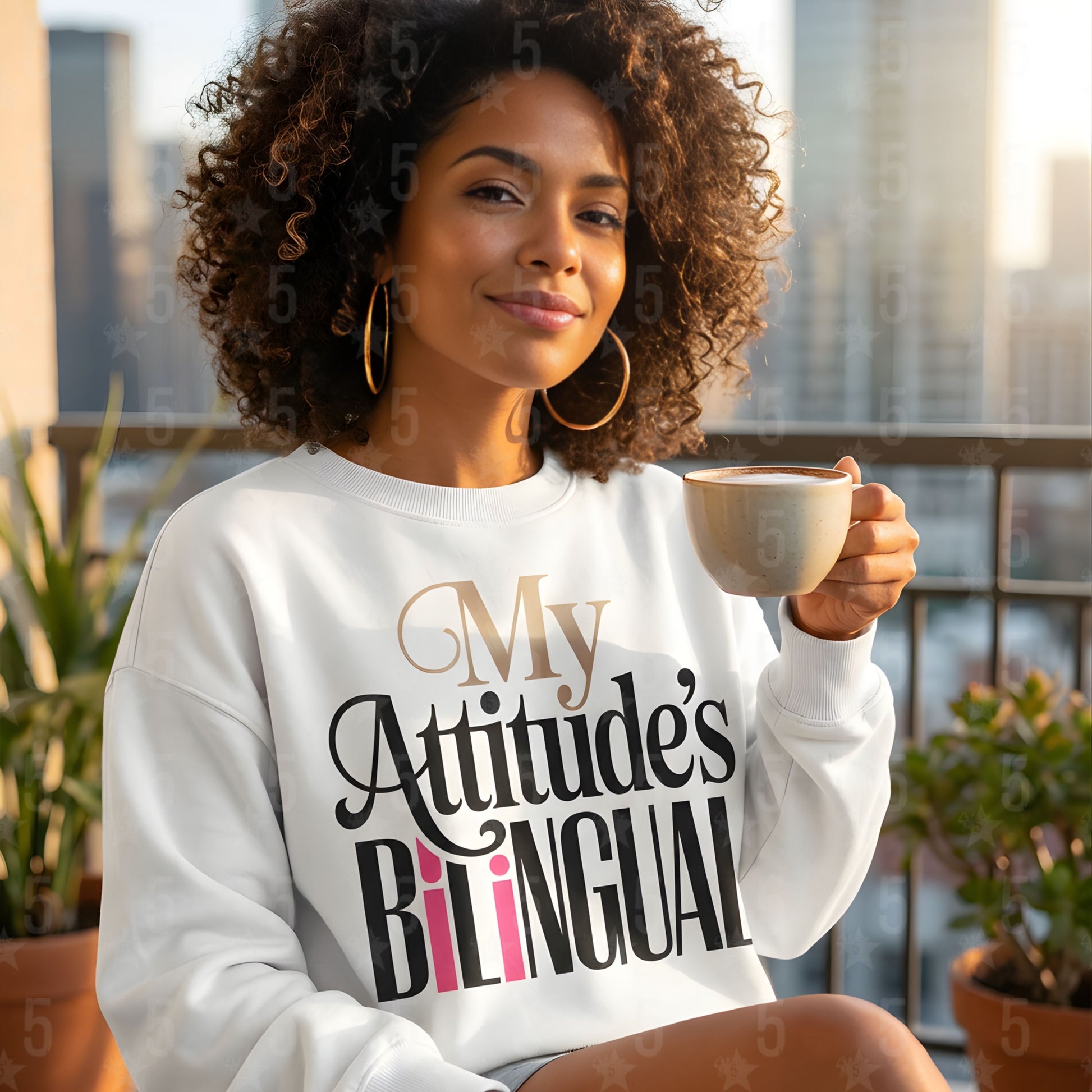 Woman wearing a sweatshirt with 'My Attitude's Bilingual' text, holding a mug on a balcony.