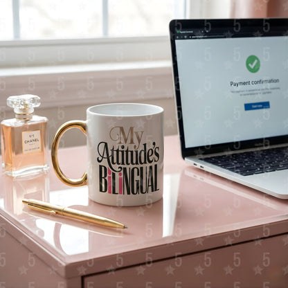 Mug with 'My Attitude's Bilingual' text on a desk next to a laptop and perfume bottle.