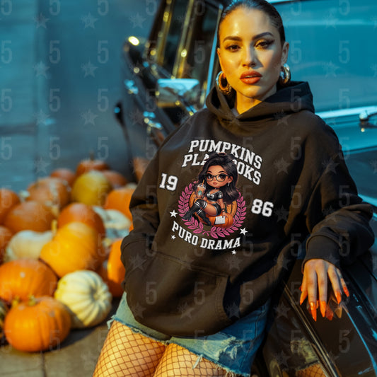 Woman wearing a black hoodie with graphic design and text, sitting in front of pumpkins.