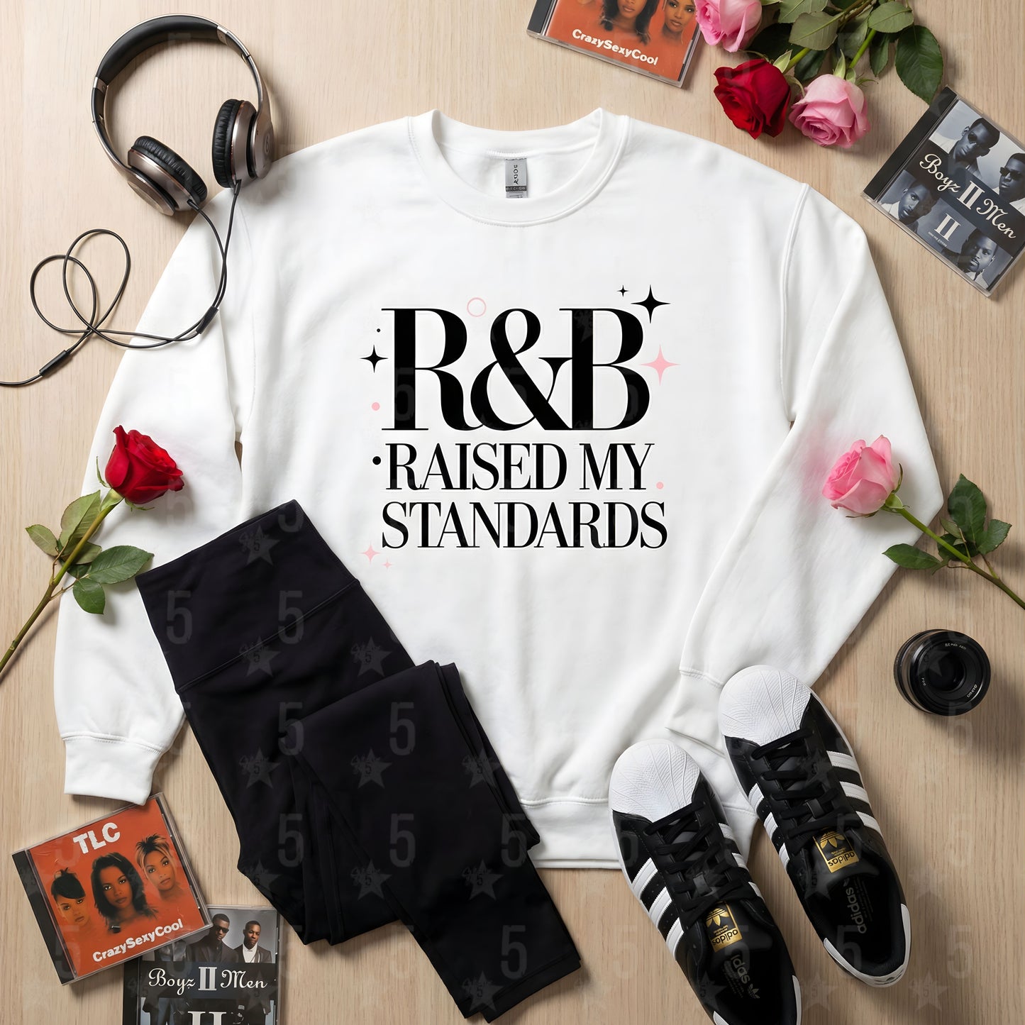 White sweatshirt with 'R&B Raised My Standards' text, black socks, Adidas shoes, headphones, and roses on a wooden surface.