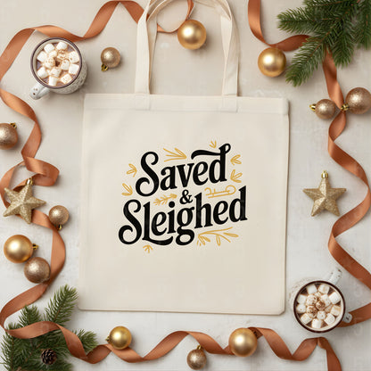 Beige tote bag with 'Saved & Sleighed' text, surrounded by Christmas decorations on a light background