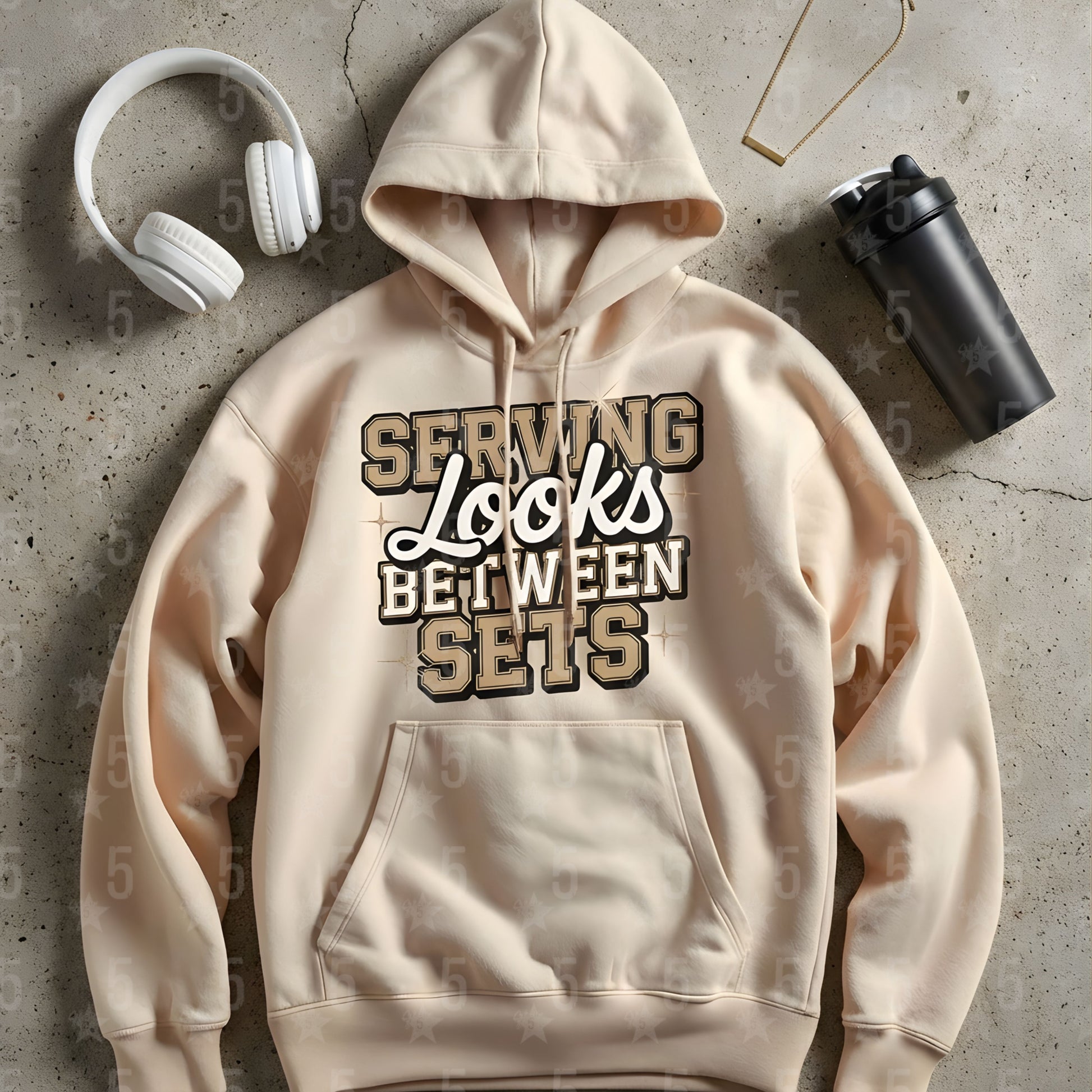 a beige hoodie laid flat on the ground with headphones. and a protein bottle shaker