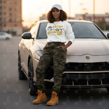 Person wearing a white sweatshirt with text, camouflage pants, and yellow boots standing next to a white car.