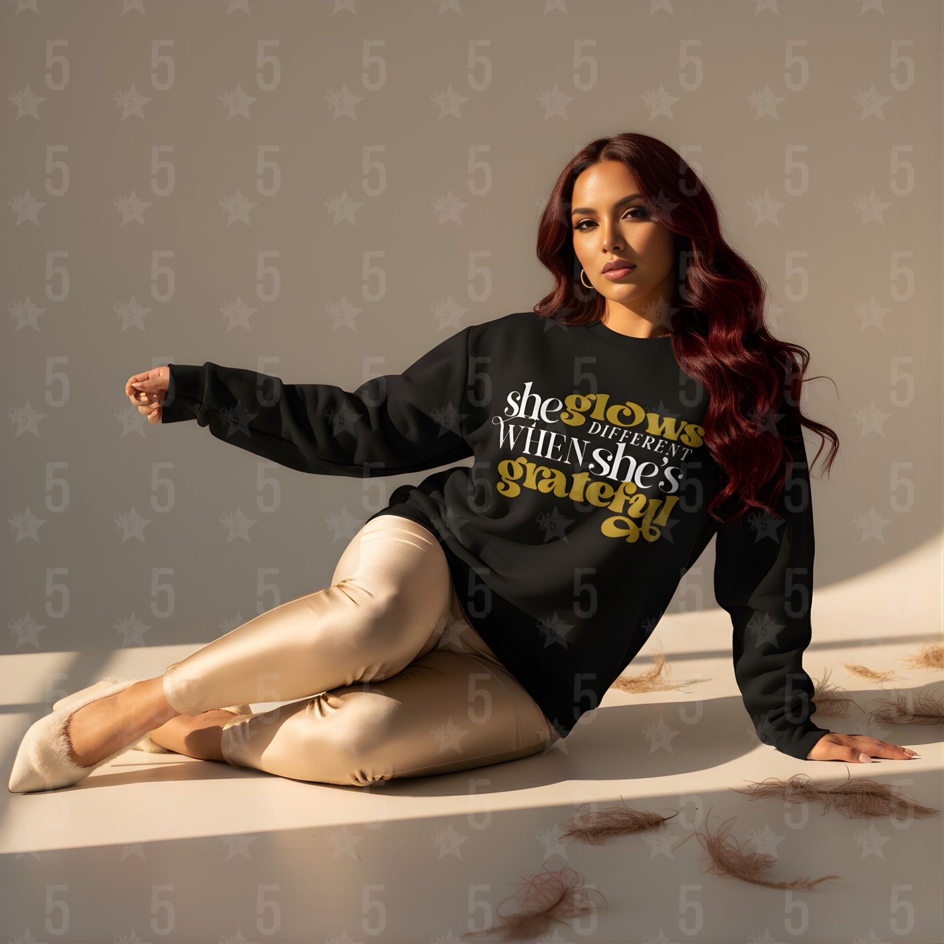 Woman wearing a black sweatshirt with text, sitting on a surface with a neutral background.